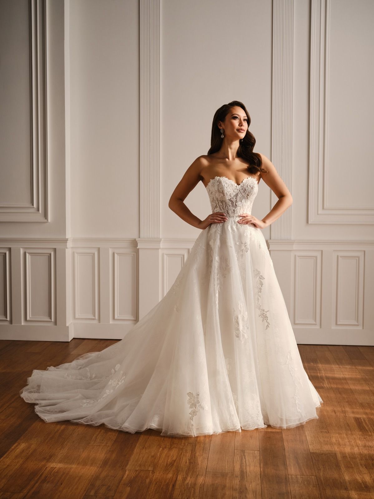 Woman in a white lace strapless gown standing in a softly lit room with paneled walls