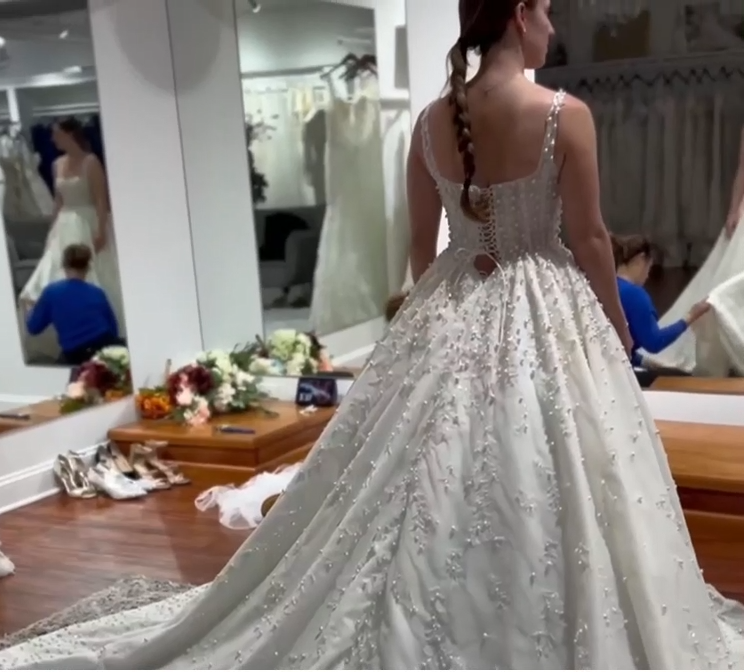 Woman in a beaded wedding dress, back to the camera, trying it on in a bridal shop. Woman in a beaded wedding dress, back to the camera, trying it on in a bridal shop.