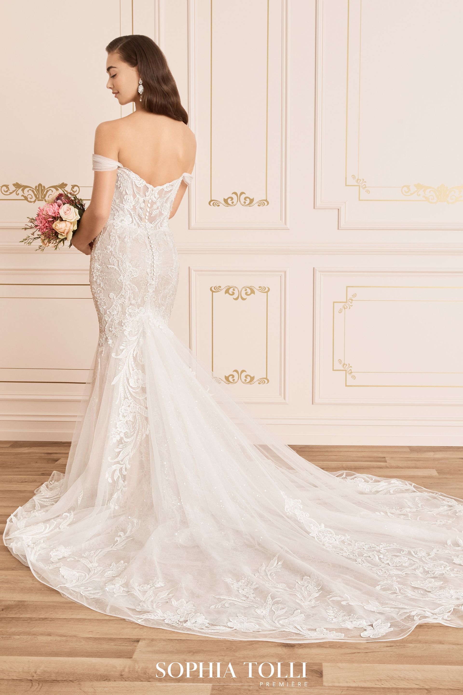 Woman in a white, off-the-shoulder wedding dress with a long veil in an outdoor setting.