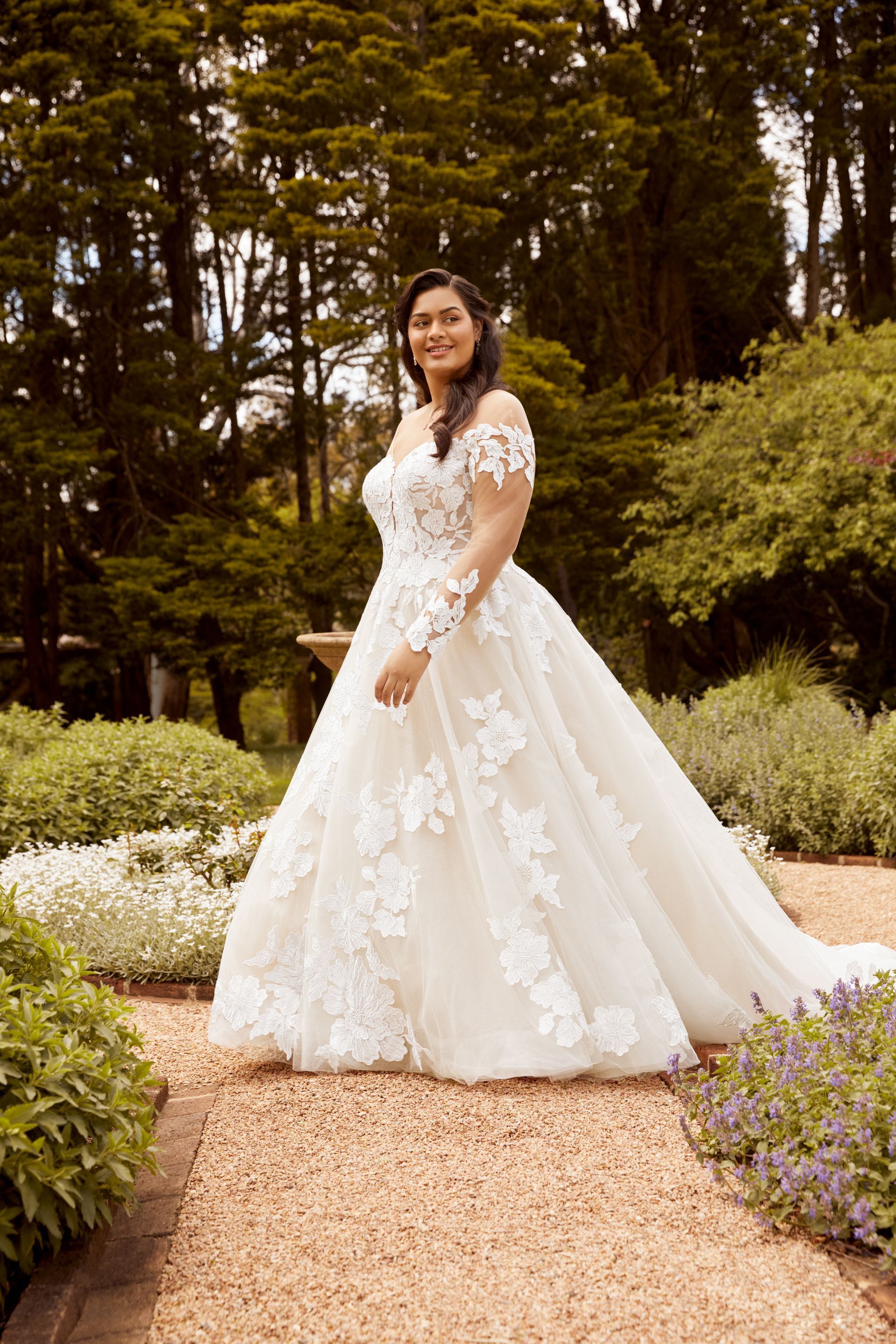 Woman in white lace wedding dress poses in garden.