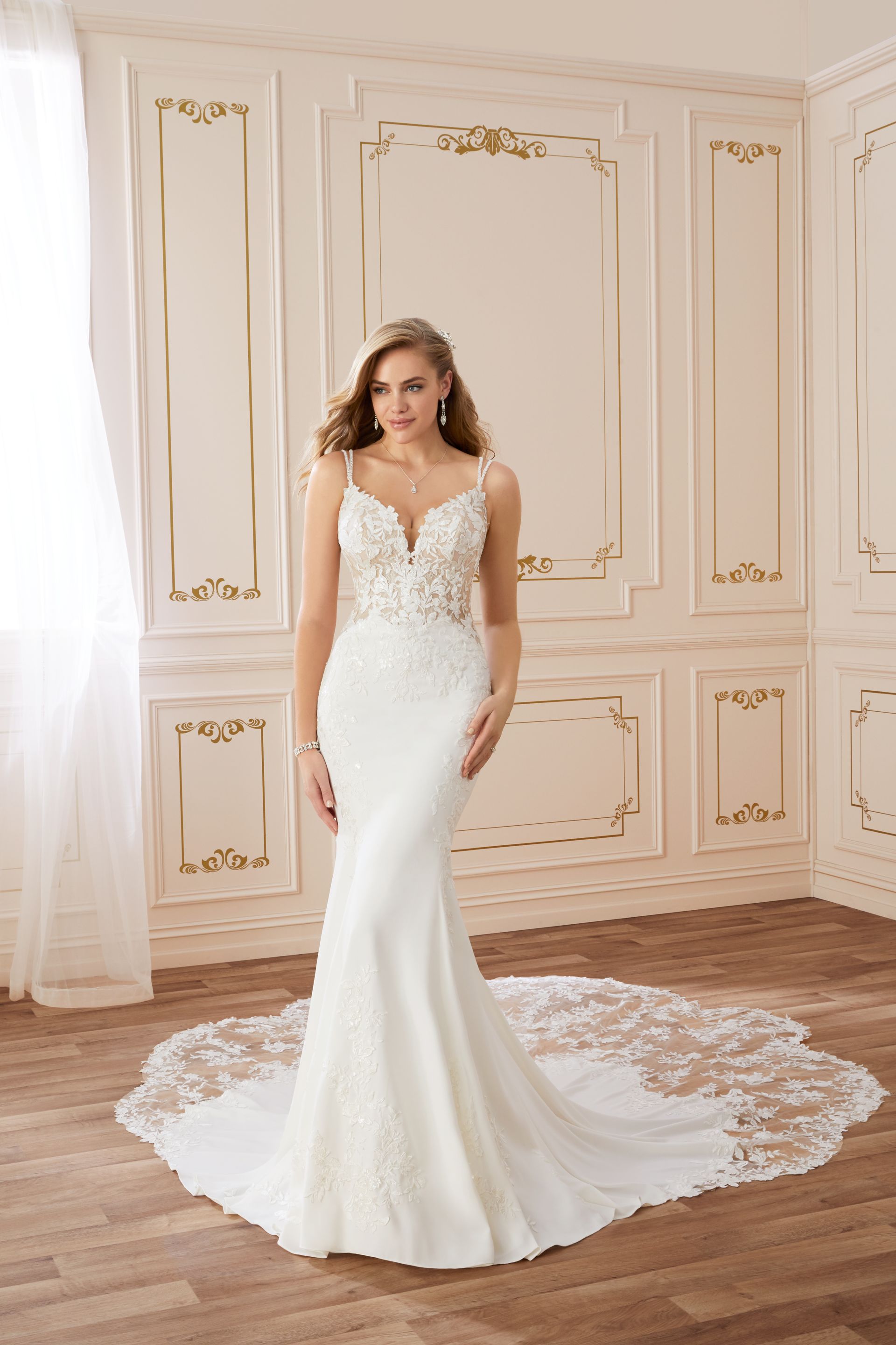 Woman in a white wedding dress with a long train, posing in a room with decorative wall panels.