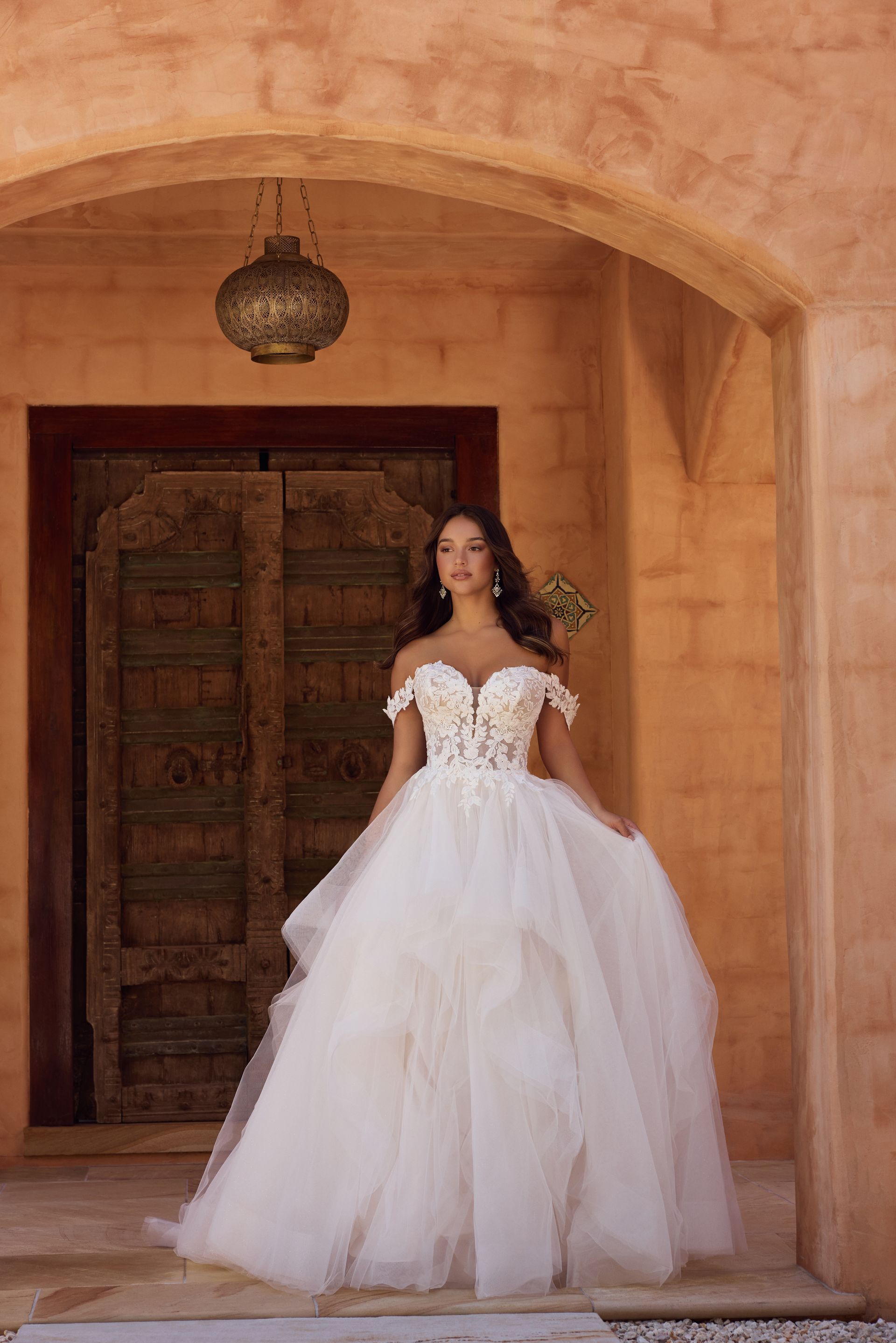 Woman in a wedding gown poses in an arched doorway with ornate wooden doors.