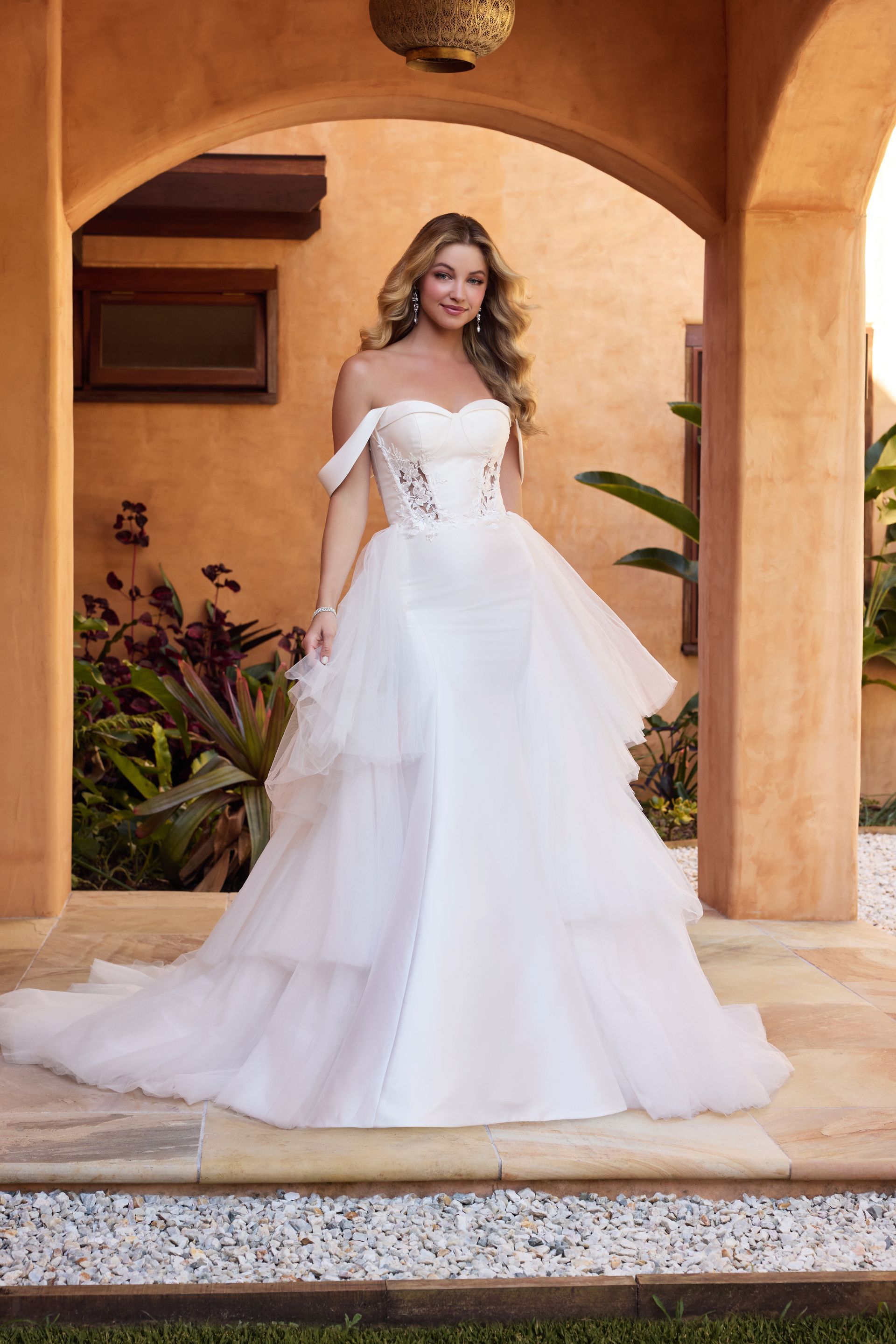 Woman in white strapless wedding gown, posing outdoors in front of a stone archway.
