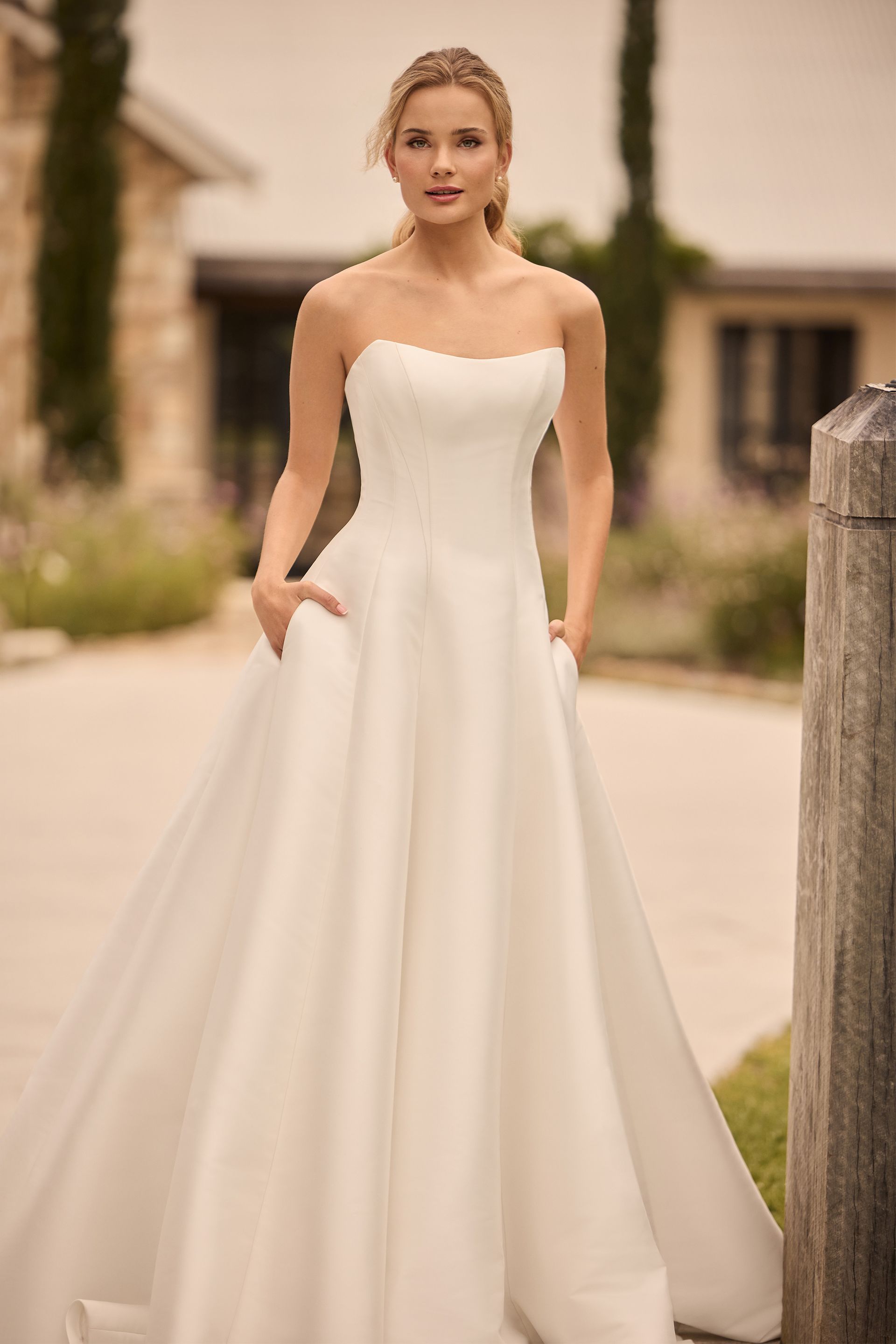 Woman in off-the-shoulder wedding gown standing outside, holding skirt.