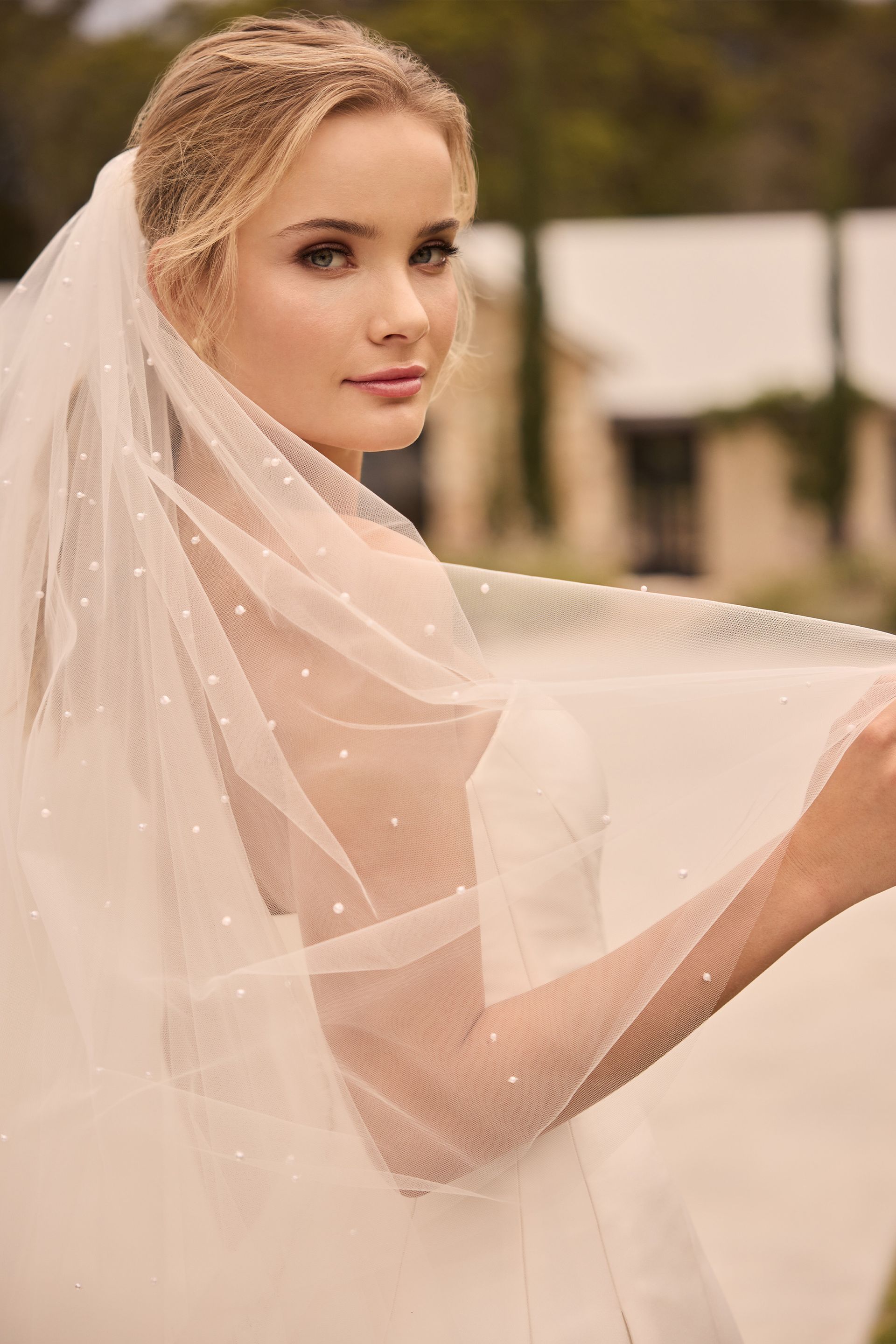 Woman in a white wedding dress and veil, looking over her shoulder.