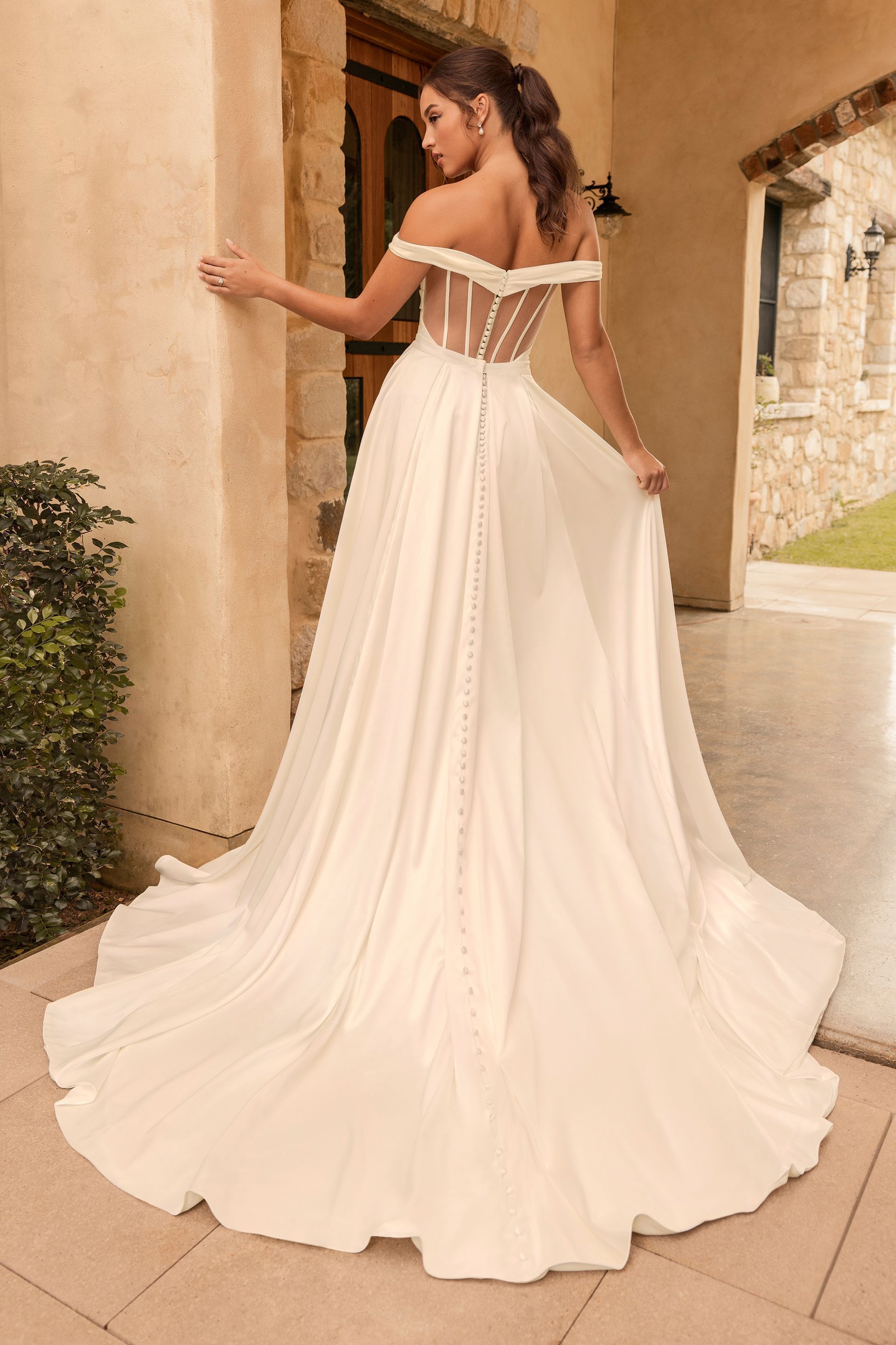 Woman in off-the-shoulder wedding dress, standing outdoors, with a long flowing skirt.