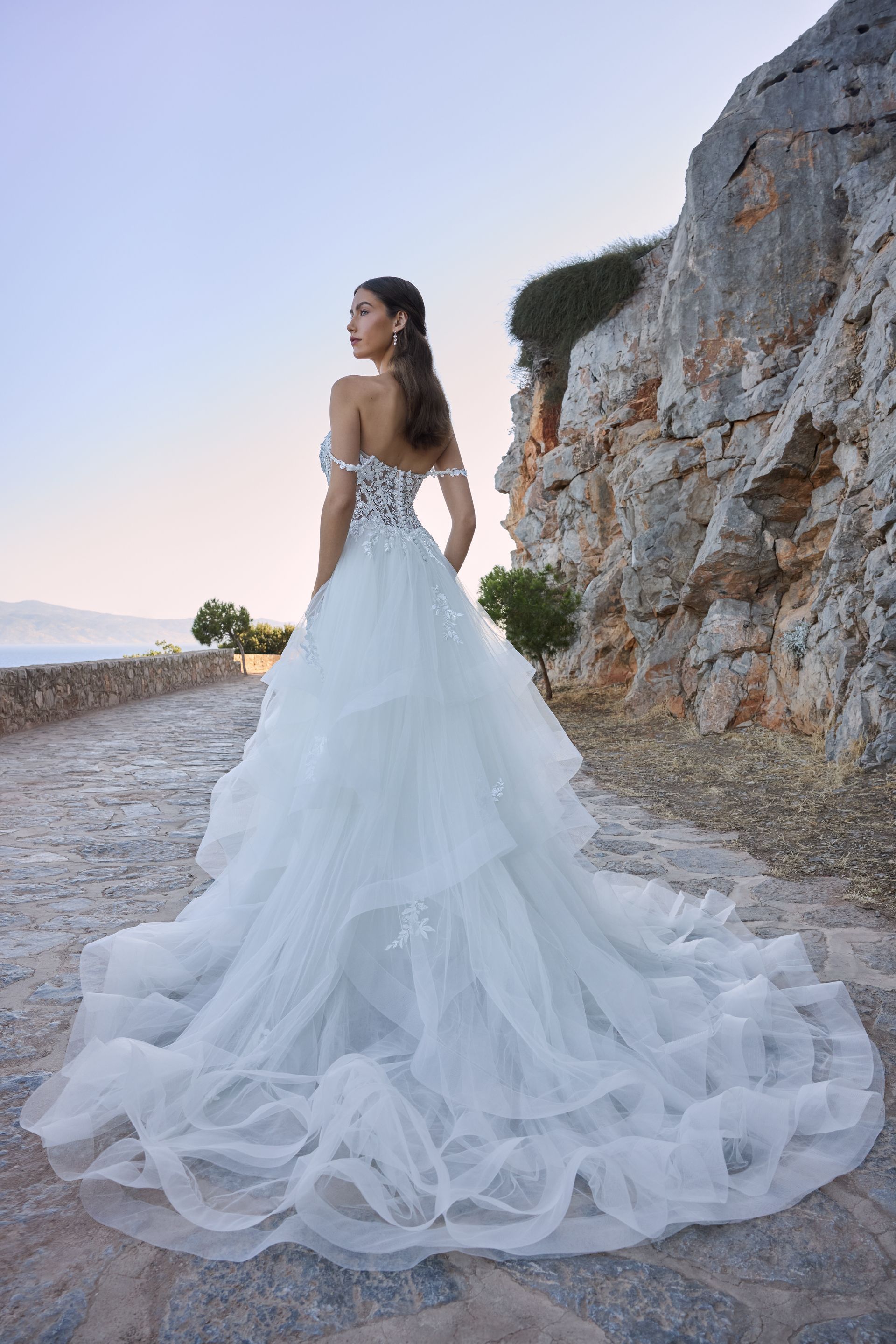 Woman in a white wedding dress stands on a stone path, looking back at the camera.