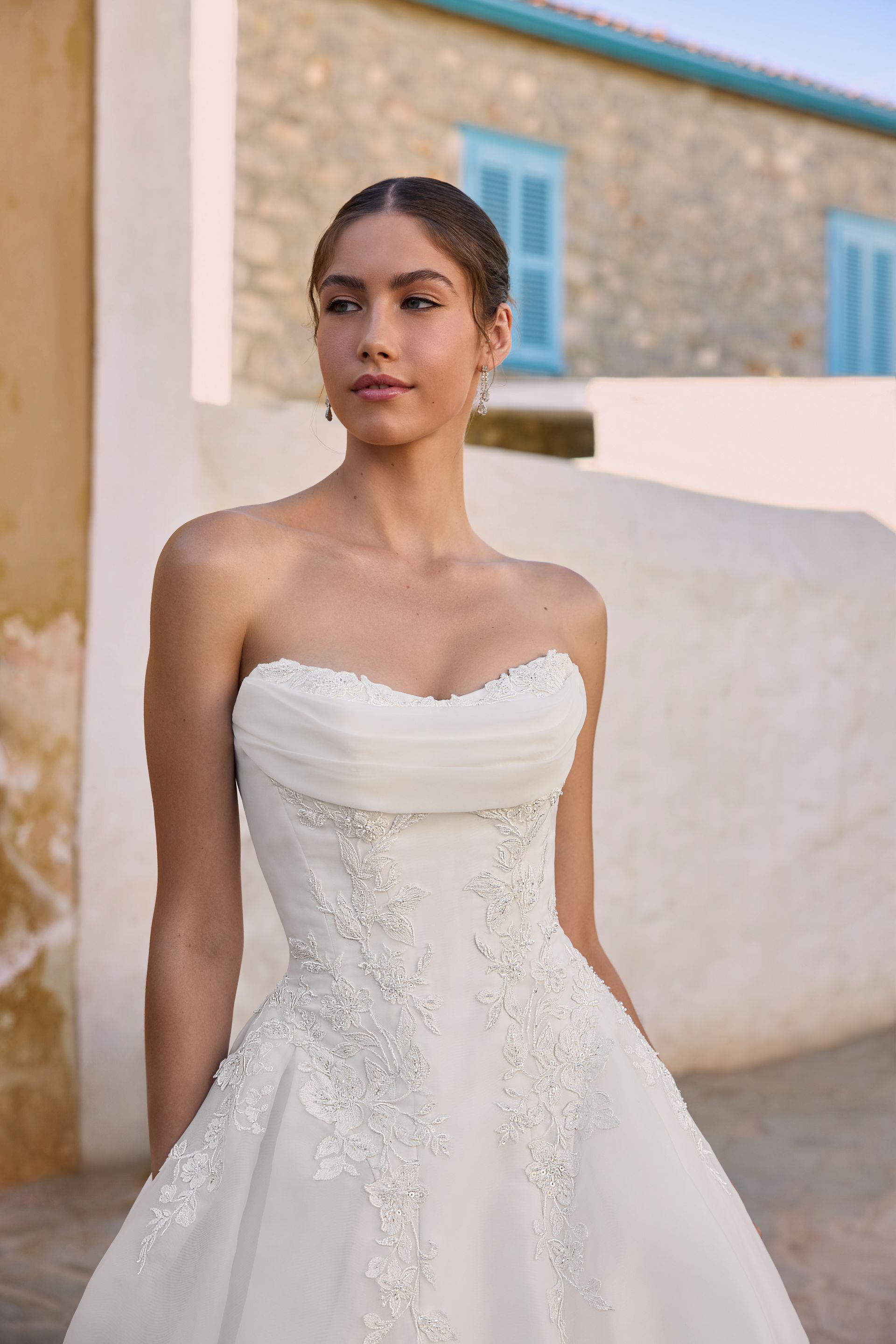 Bride in strapless white gown, standing outside a building with blue shutters.