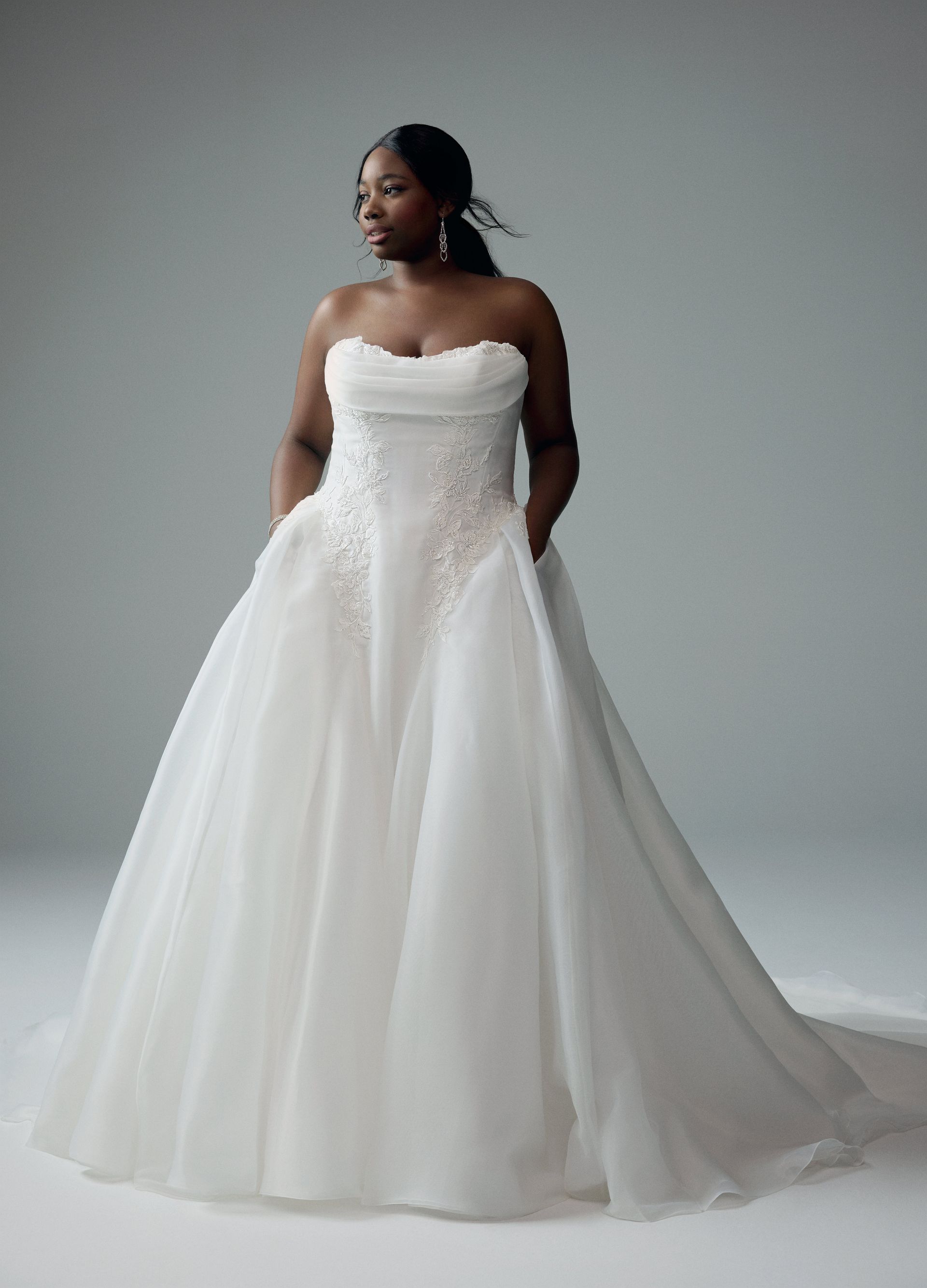 Woman in strapless white wedding dress with pockets, standing against a neutral background.