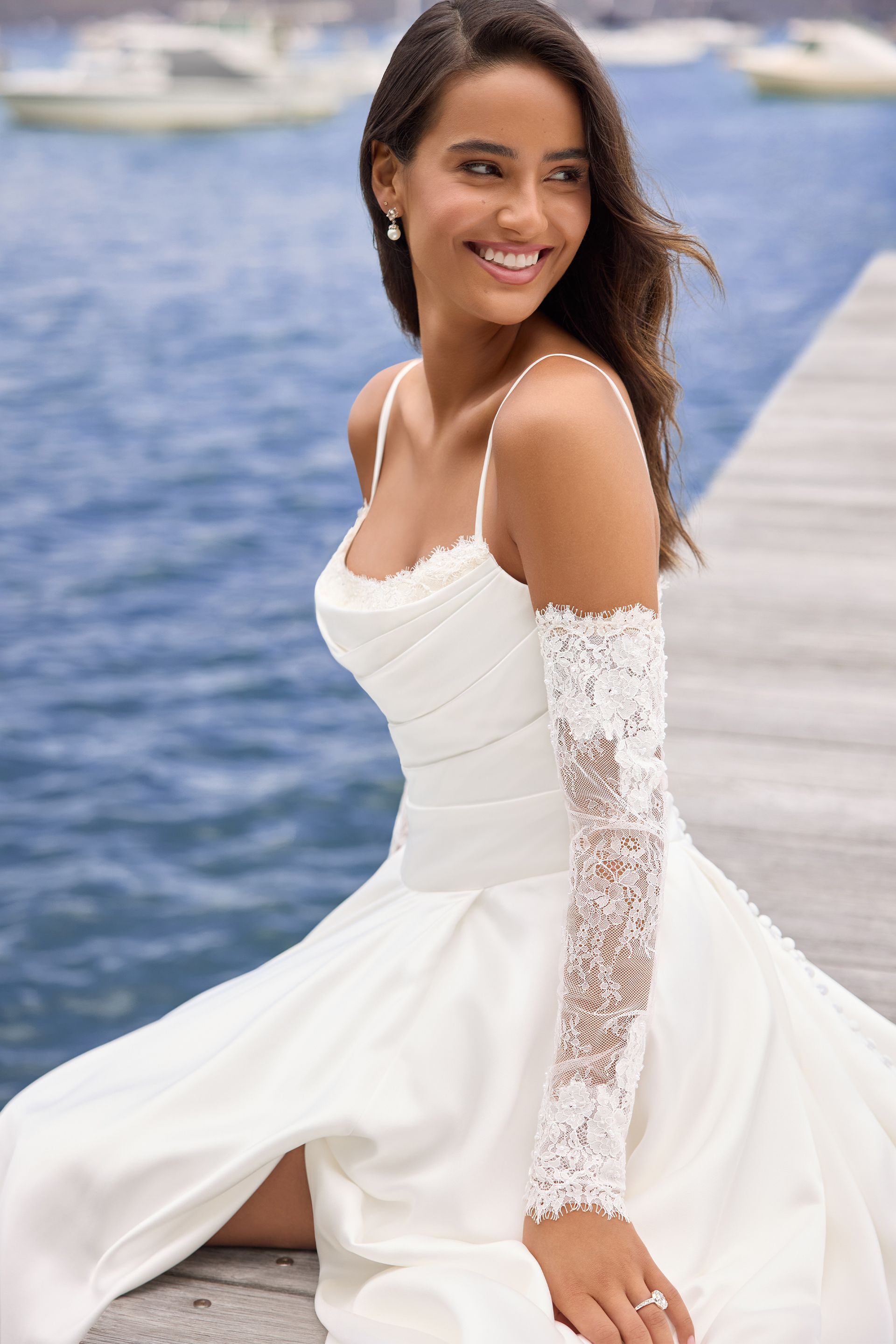 Woman in white wedding dress with lace sleeves, standing outdoors, blue sky background.