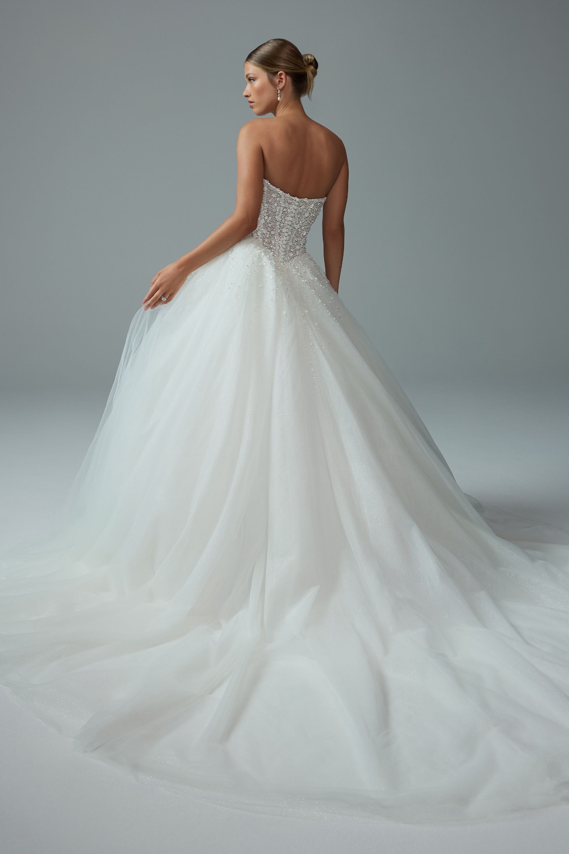 Woman in a white strapless wedding gown with a full skirt and train, standing in a studio.