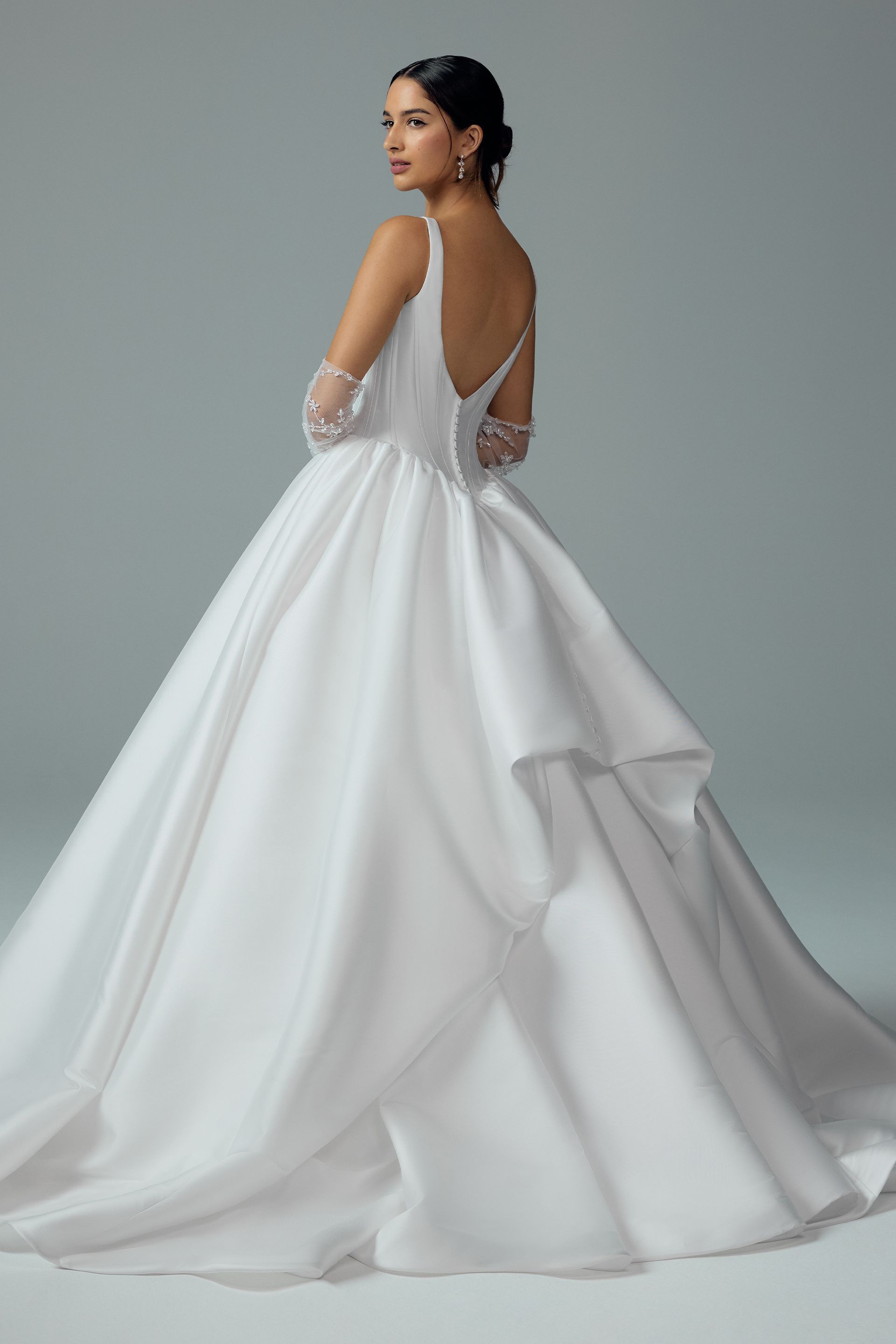Woman in a white satin wedding gown, turned toward the camera, open back, ballgown skirt.