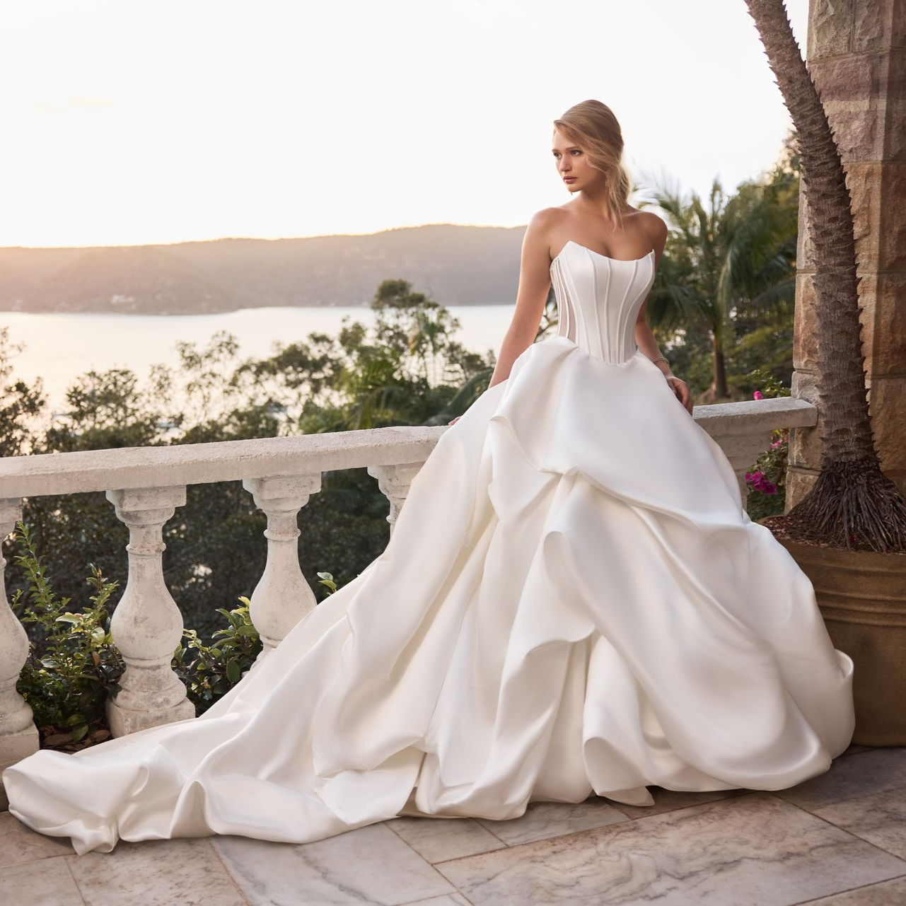 Woman in a white strapless ballgown poses on a balcony overlooking the water at sunset. Woman in a white strapless ballgown poses on a balcony overlooking the water at sunset.