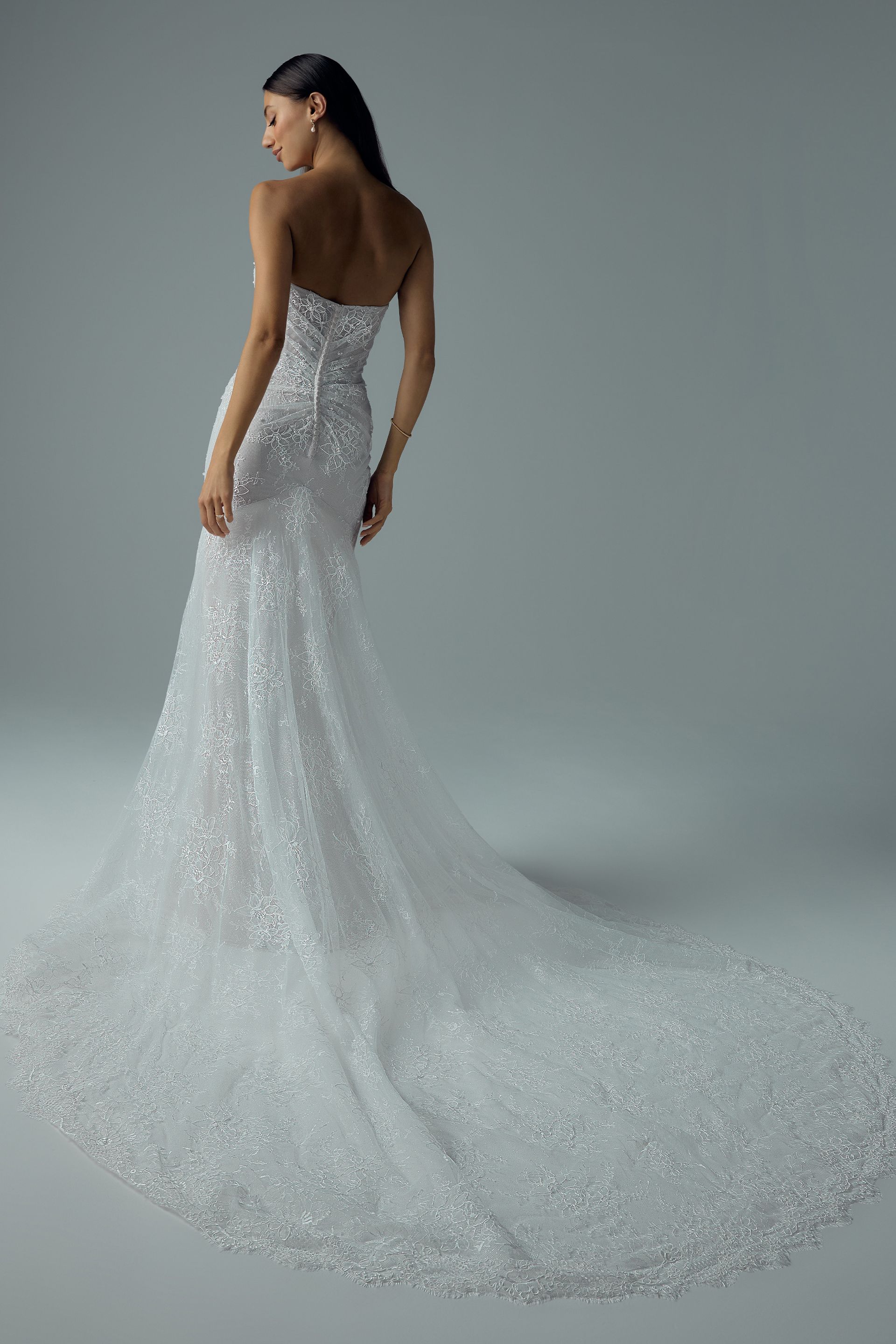 Woman in a strapless lace wedding gown standing by a large window in a bright room