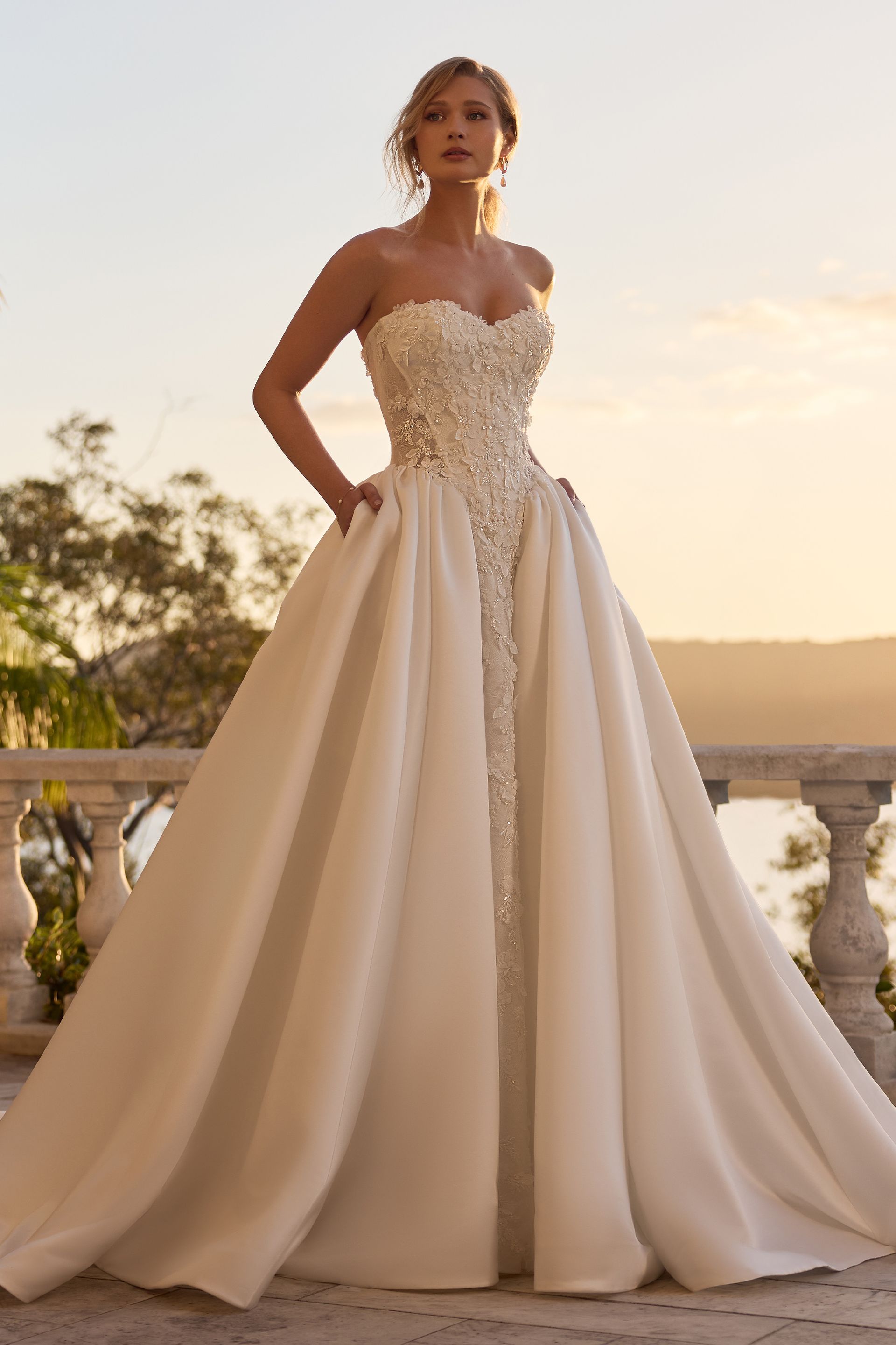 Woman in a strapless white gown standing on a balcony at sunset