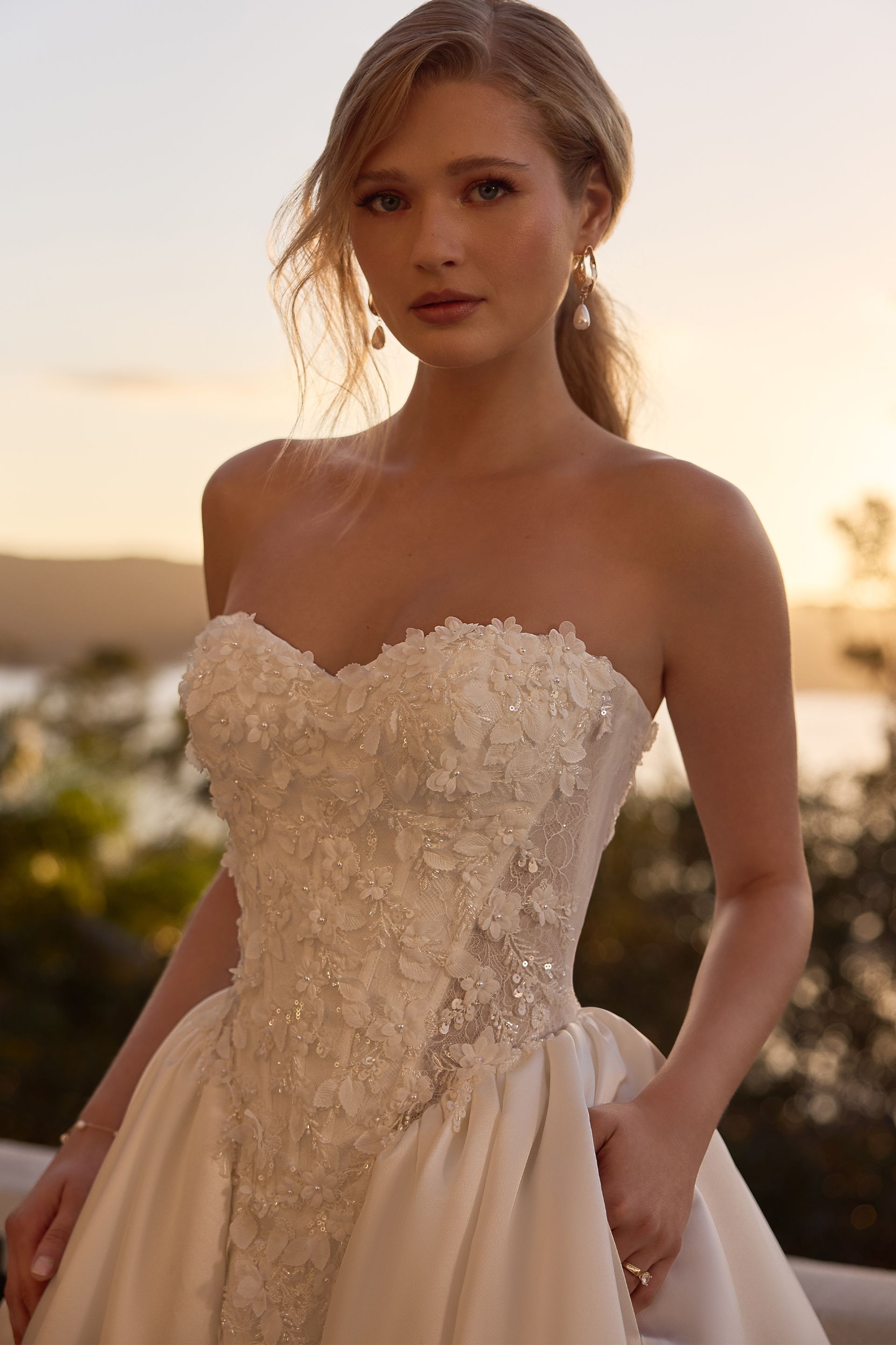 Woman in a strapless white gown standing on a balcony at sunset