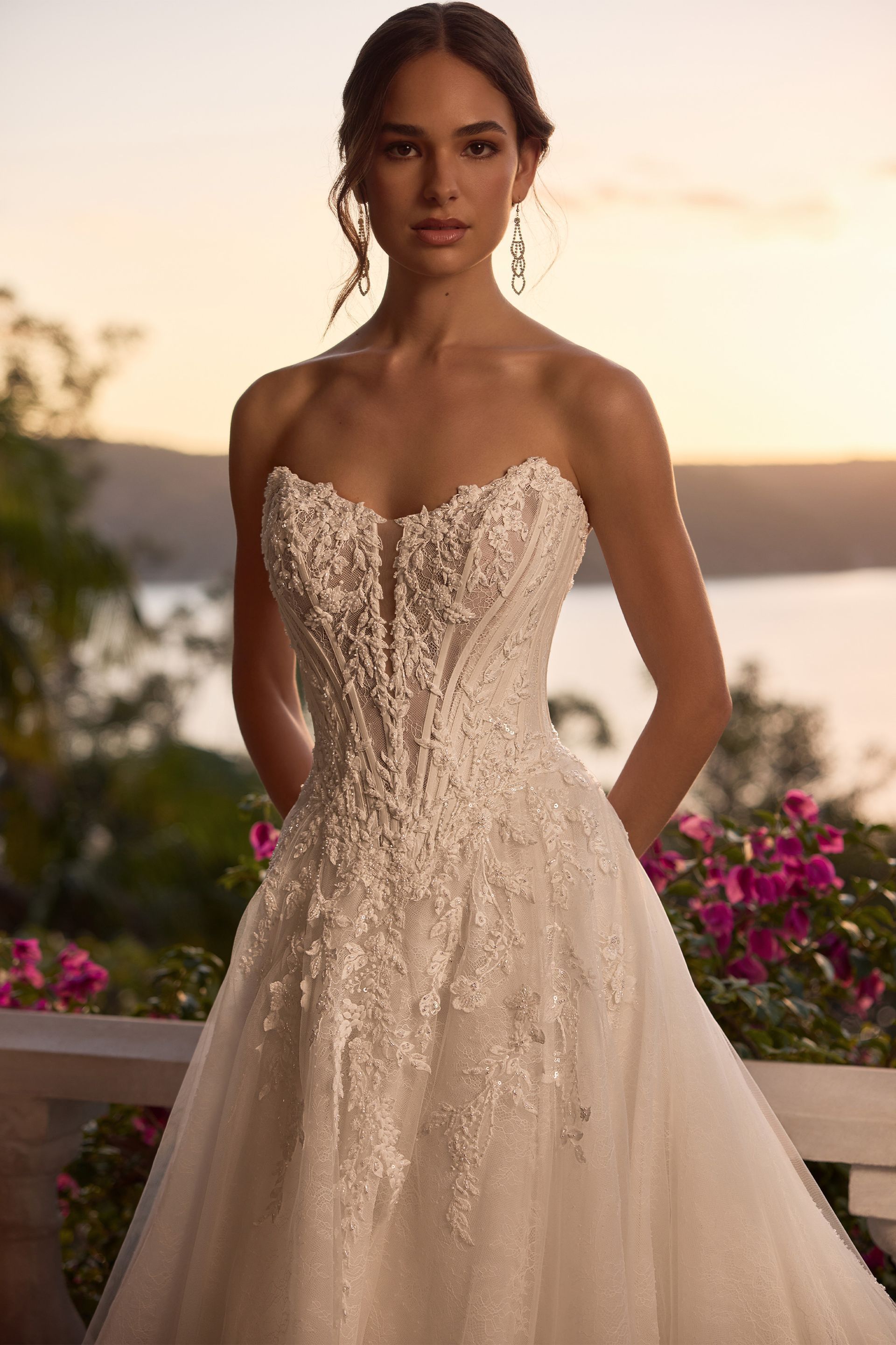 Woman in a strapless white wedding dress with beading, standing outdoors at sunset.