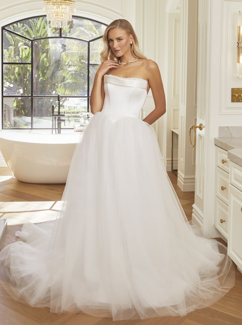 Woman in a strapless white wedding dress in a bright bathroom with a tub.