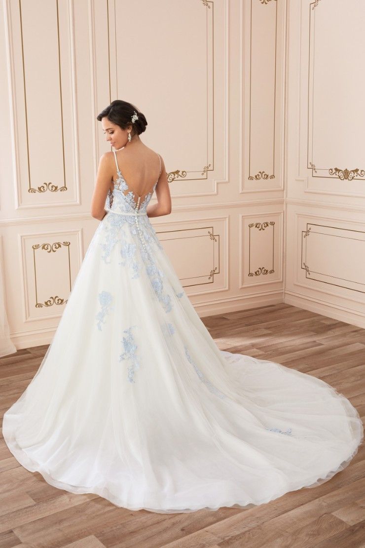 Woman in white wedding dress with blue floral accents, standing in a room with decorative wall panels.