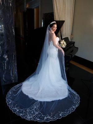 Bride in a white mermaid gown with a long veil, standing near a black grand piano. Bride in a white mermaid gown with a long veil, standing near a black grand piano.