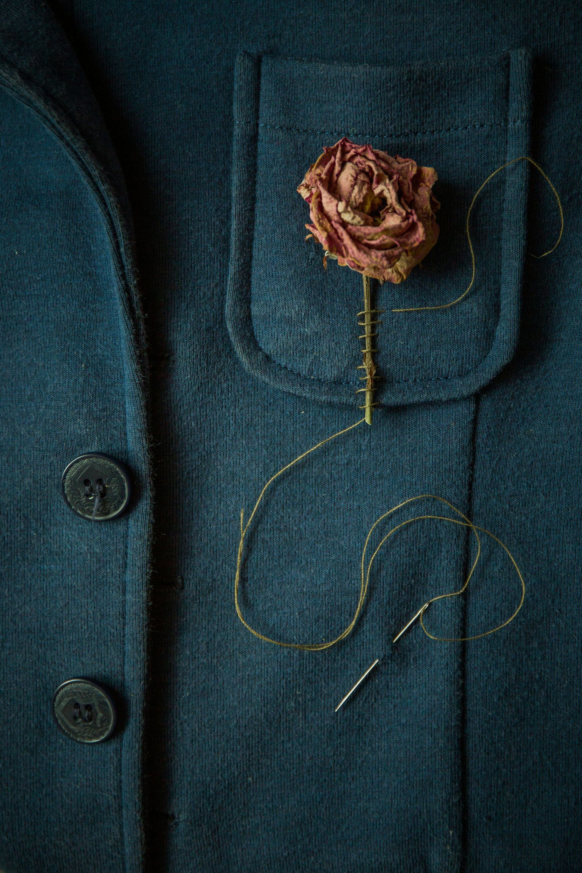 Blue jacket with dried rose in pocket, needle and thread nearby.