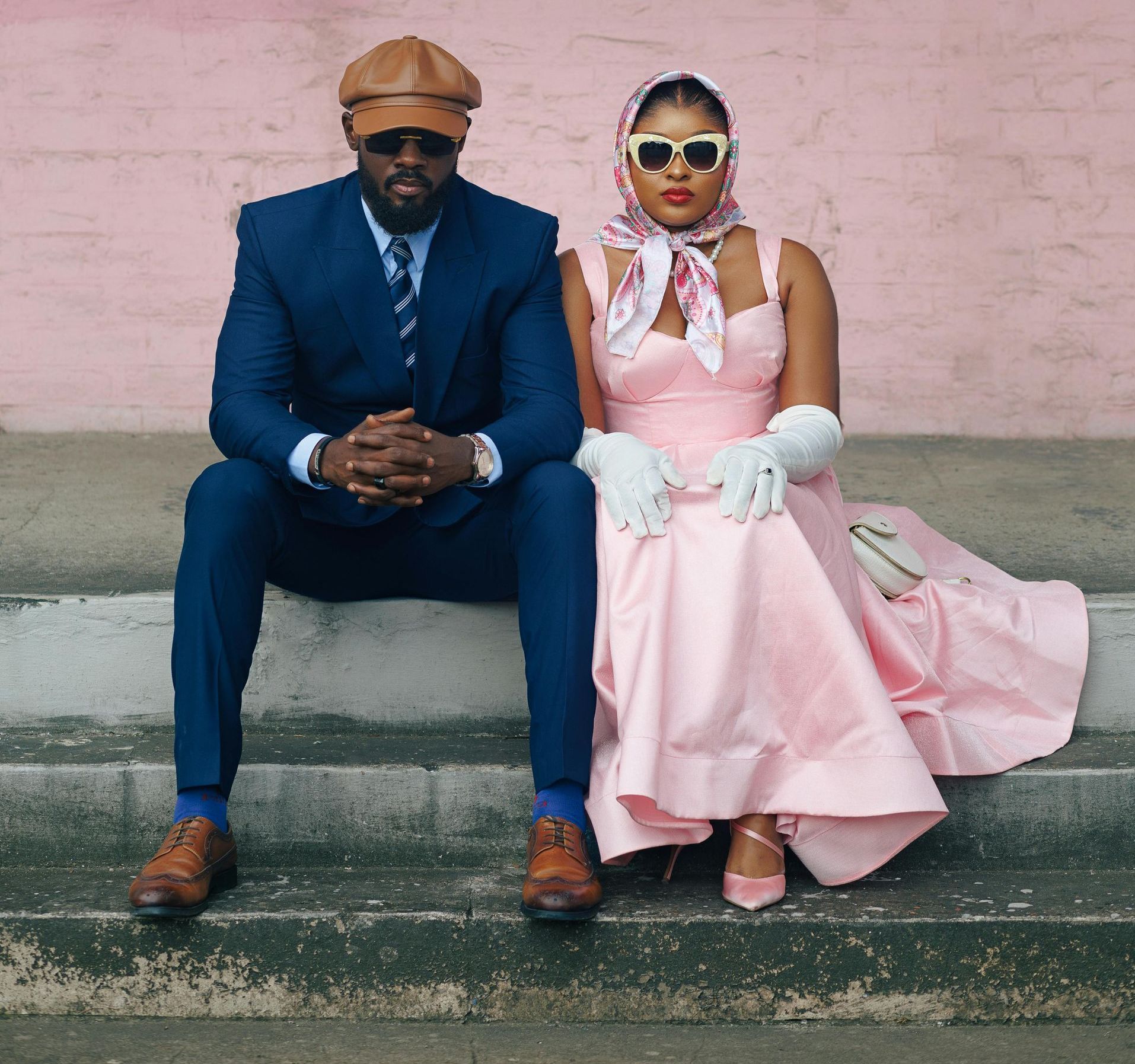Man in blue suit and woman in pink dress sit on steps, posing.