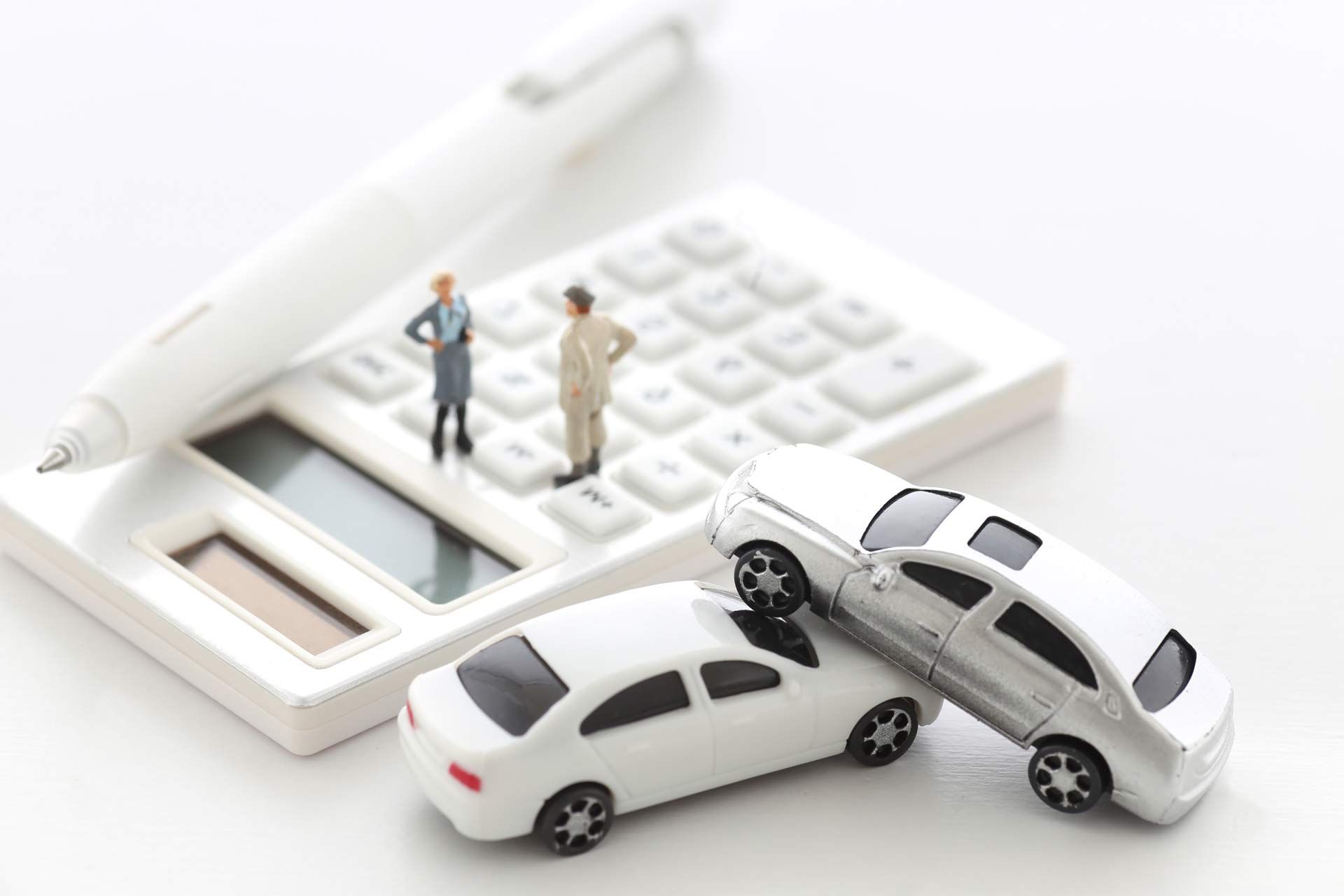 Two model figures on top of a calculator with a pen and two model cars on top of each other.