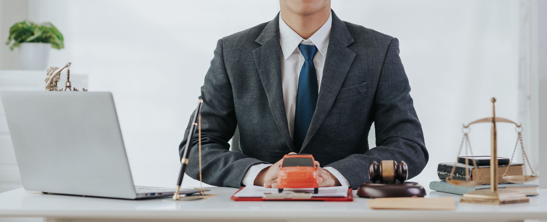 A vehicle accident lawyer seated in his office, with an orange car, documents, and a hammer.