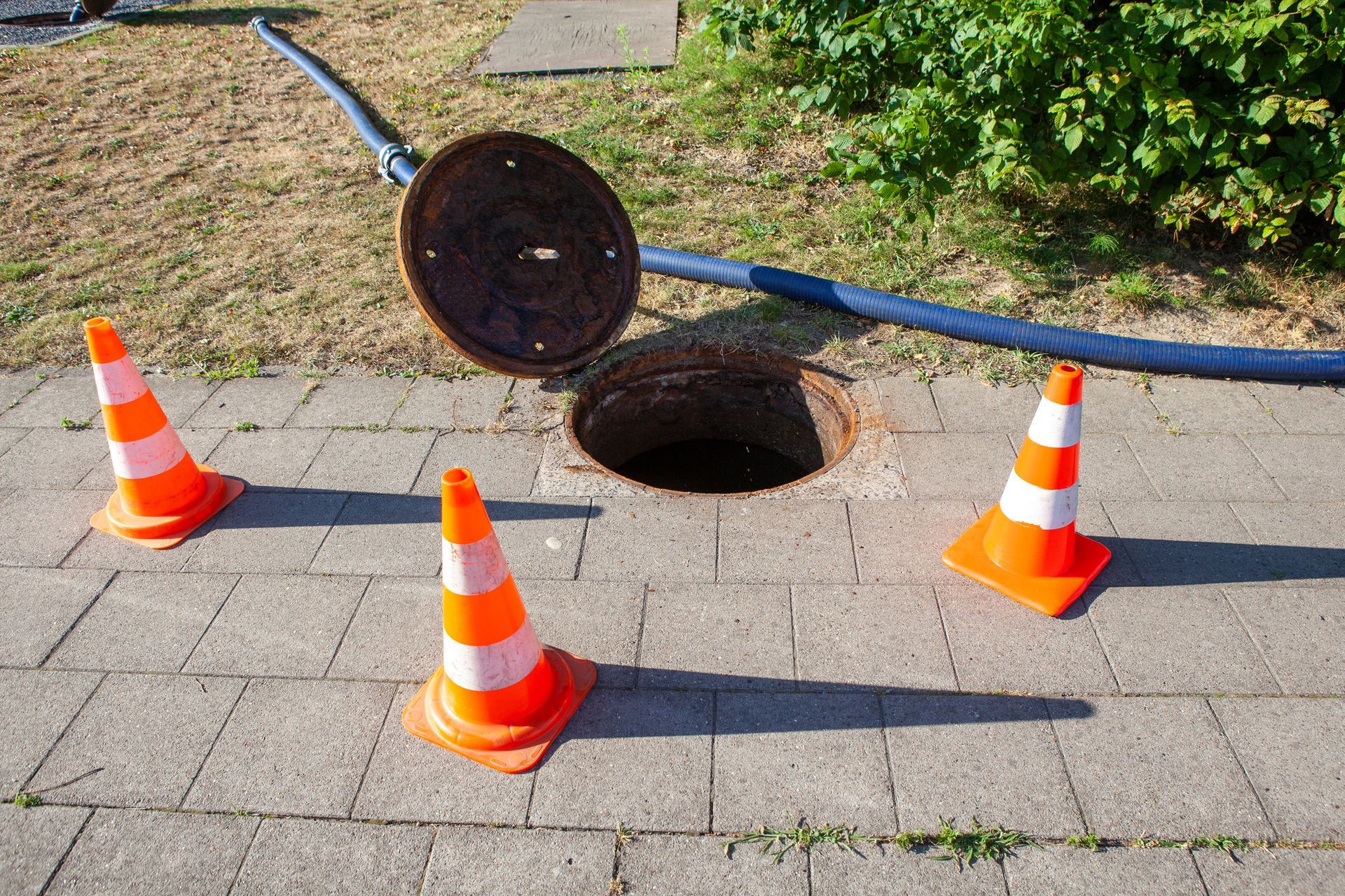 Open manhole with cones on sidewalk.