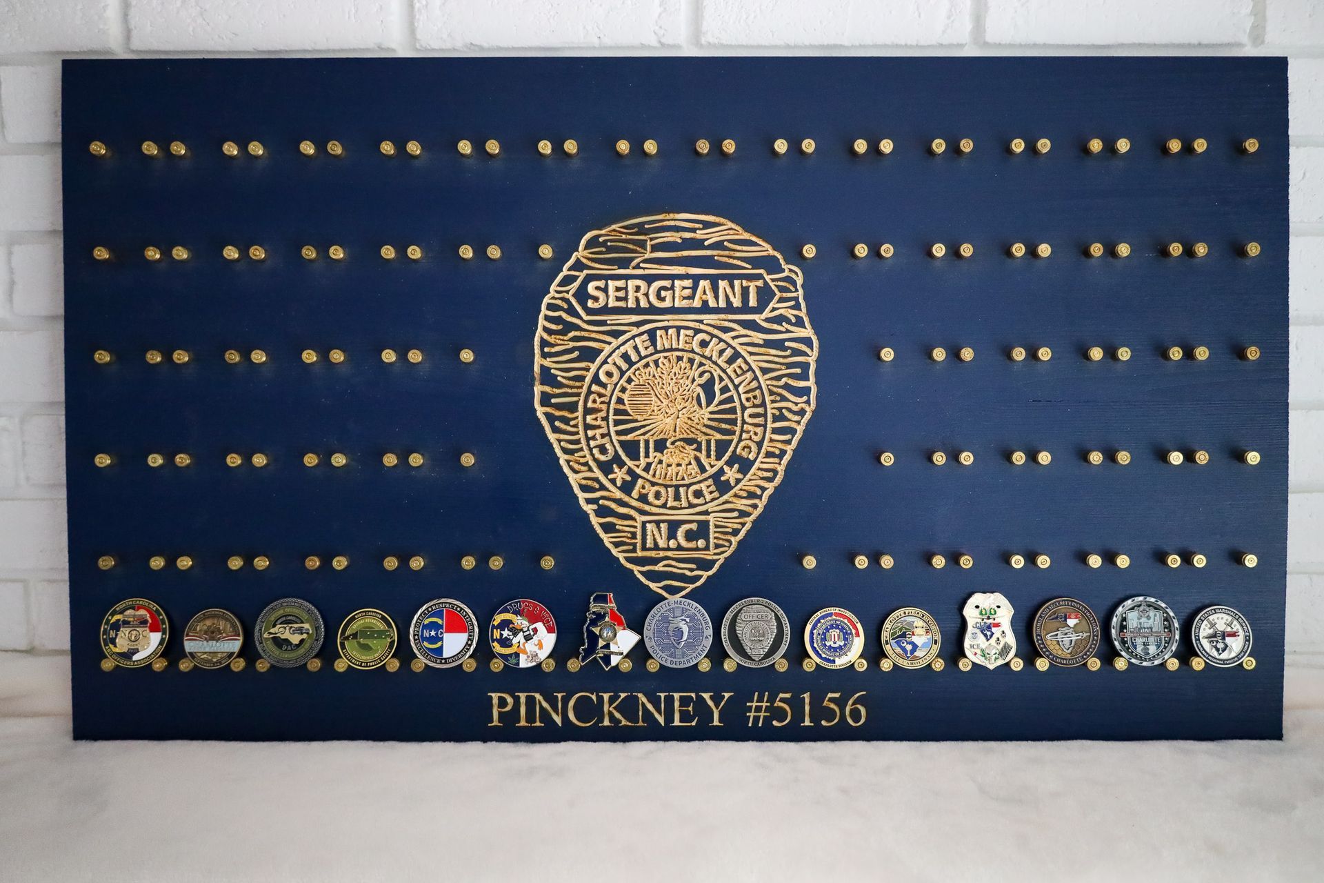 Navy-blue wooden display board with sergeant badge design and coin collection. Name and number below.