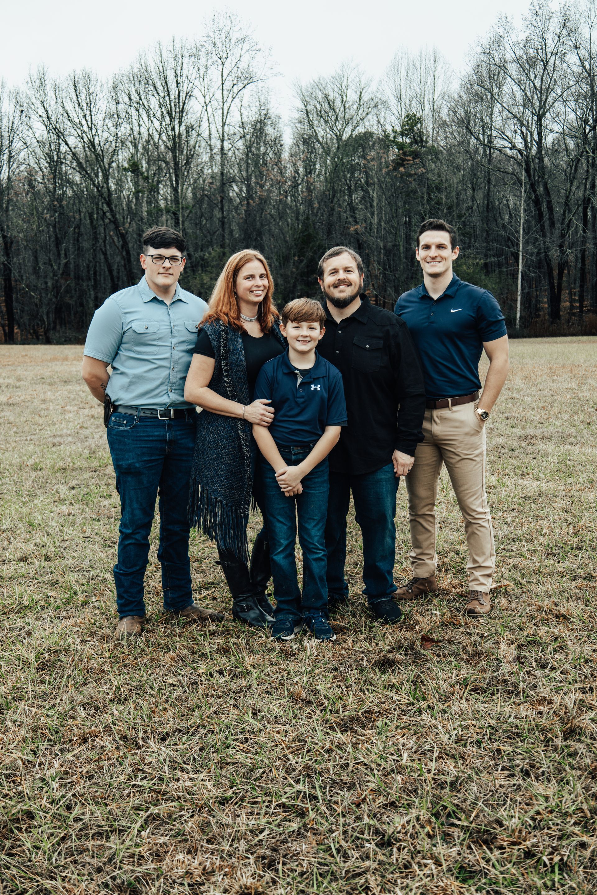 Family of five standing in a field; trees in the background. They are smiling at the camera.