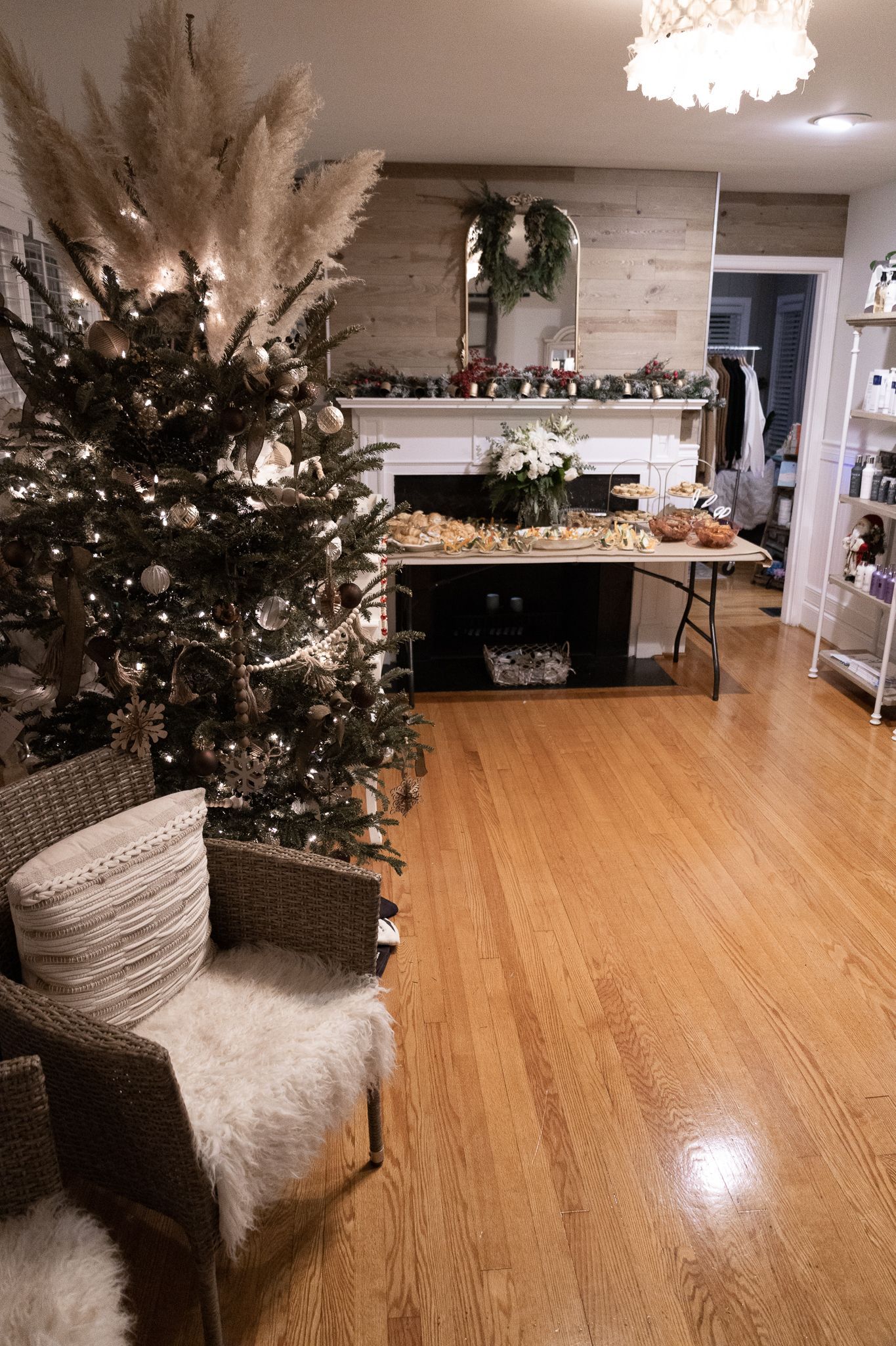 Christmas tree next to wicker chairs in a room with a decorated fireplace and a table of food.