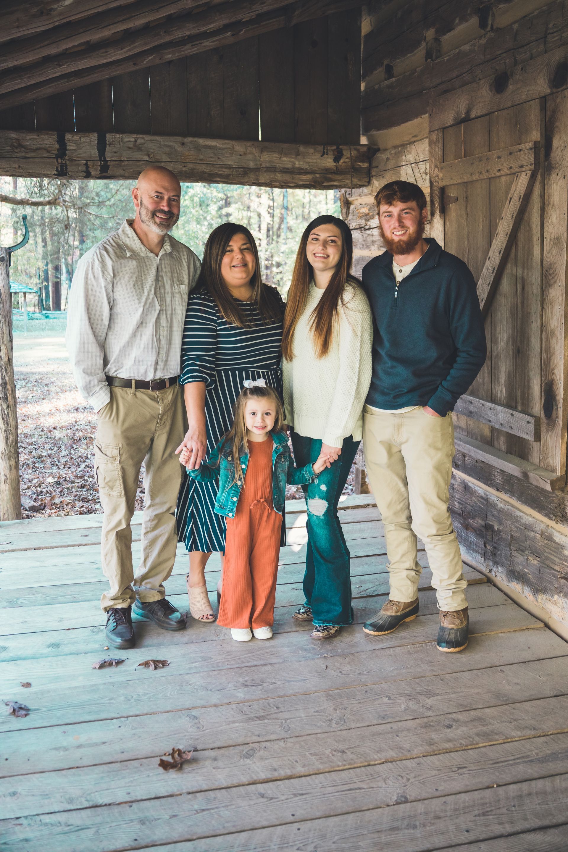 Family of five posing on a wooden porch, smiling.