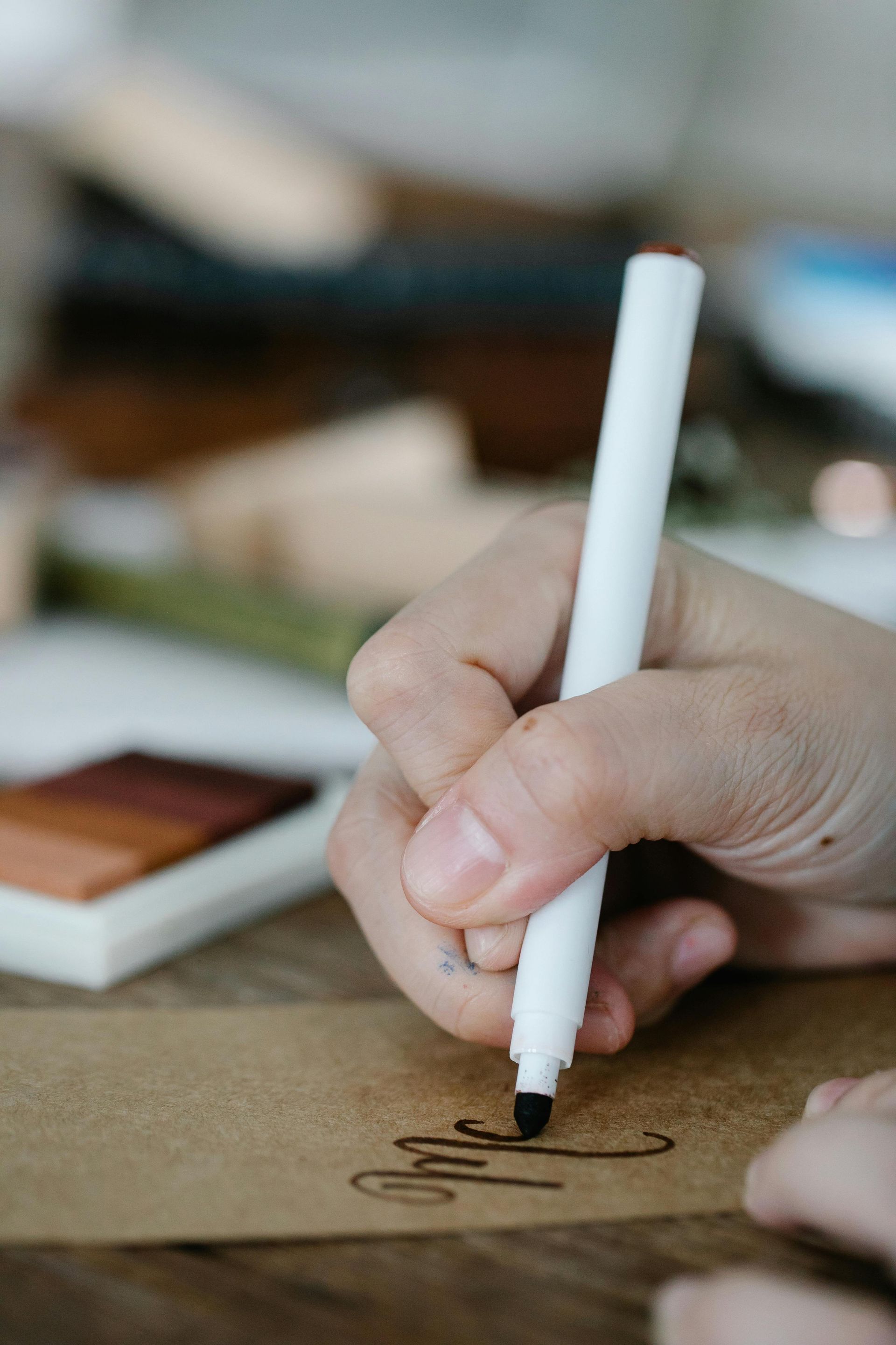 Hand writing with a white marker on brown paper, wooden table, close-up.