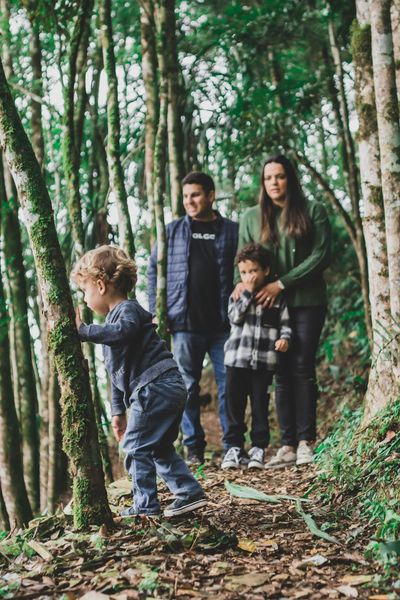 Four people standing on a forest trail among tall trees, with one child in the foreground walking ahead.