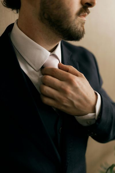 Man in a dark suit adjusting a pink tie, close-up side view indoors
