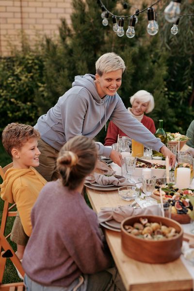 People gathered around a long outdoor dining table, sharing a meal under string lights.