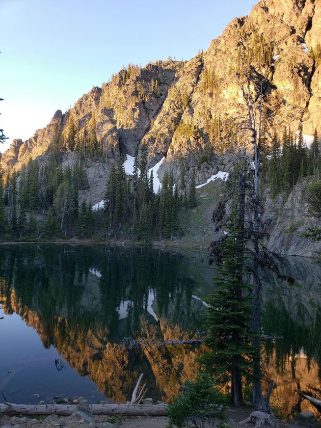 Sunlit mountain reflected in a calm lake with pine trees along the shore