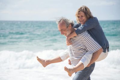 Man carrying a smiling child on his back at the beach with ocean waves in the background