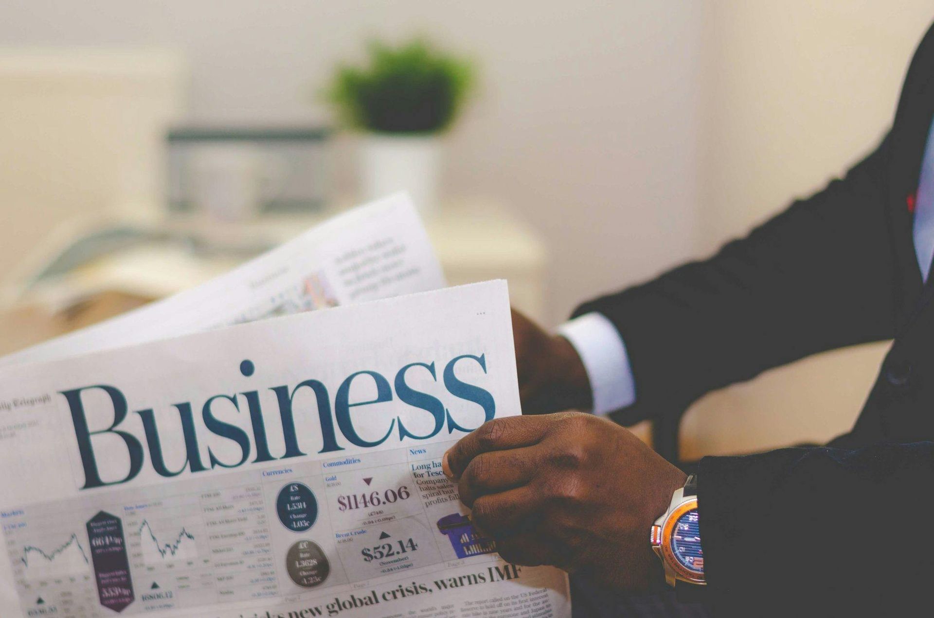 Person holding a newspaper with the headline “Business” in a bright office setting
