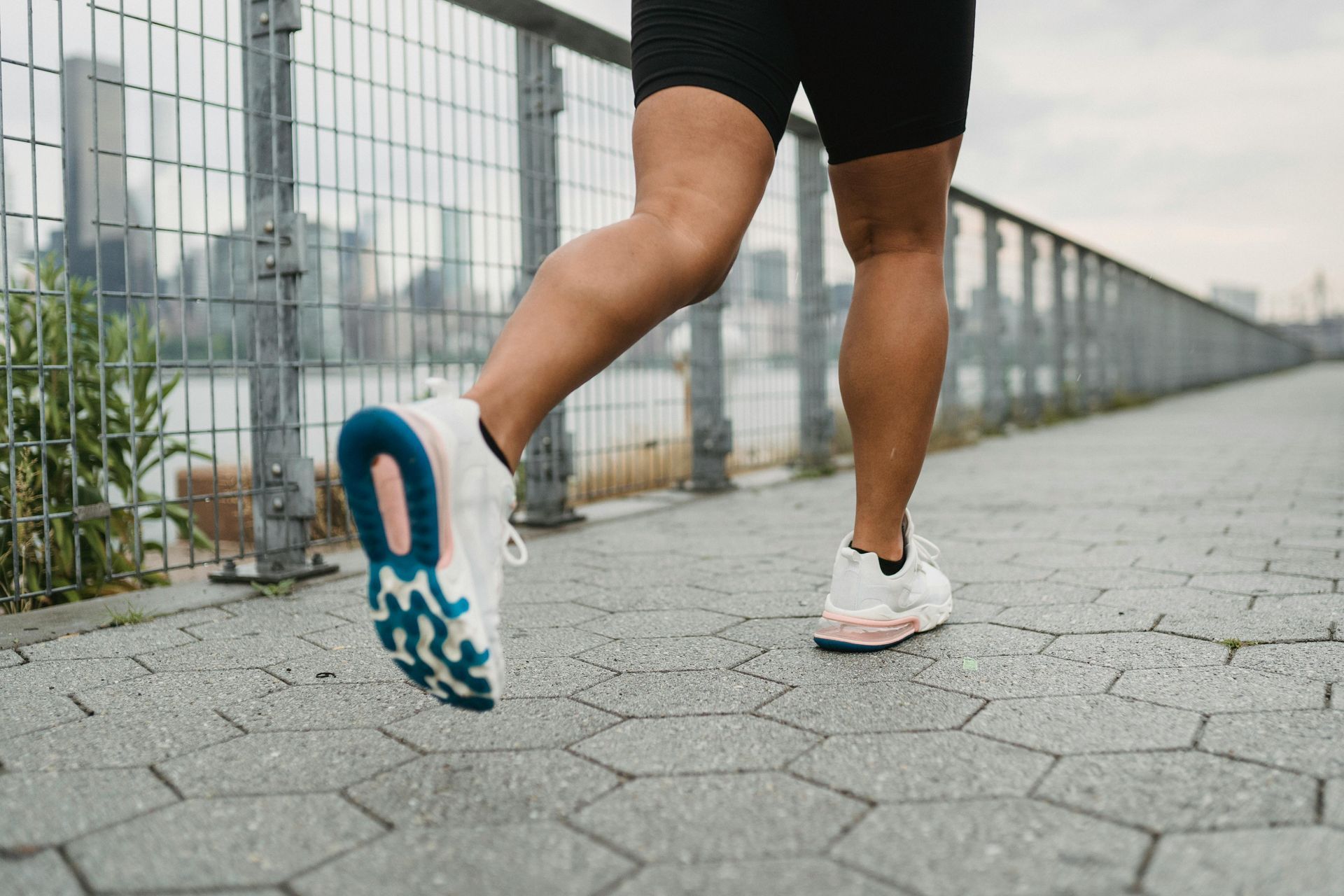 Person running on a path with city in background. Wearing black shorts and white sneakers with blue and pink accents.