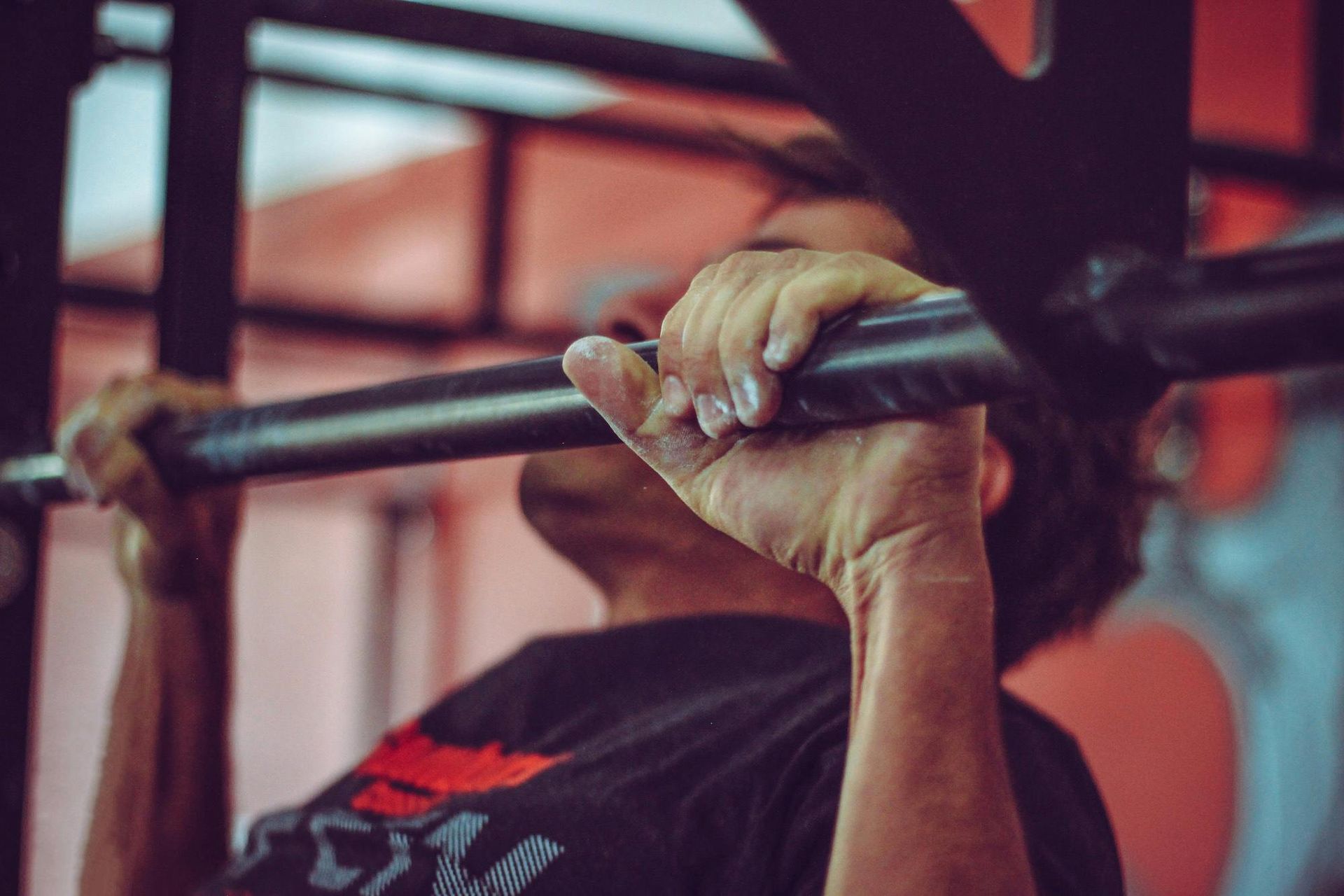 Person doing a pull-up on a black bar in a gym; red and black setting.