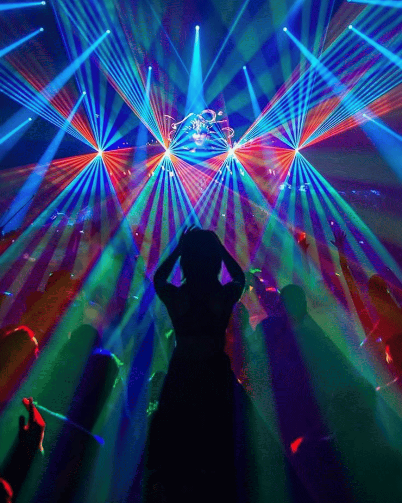 Silhouette of a person with hands on head in a club lit by colorful lasers.
