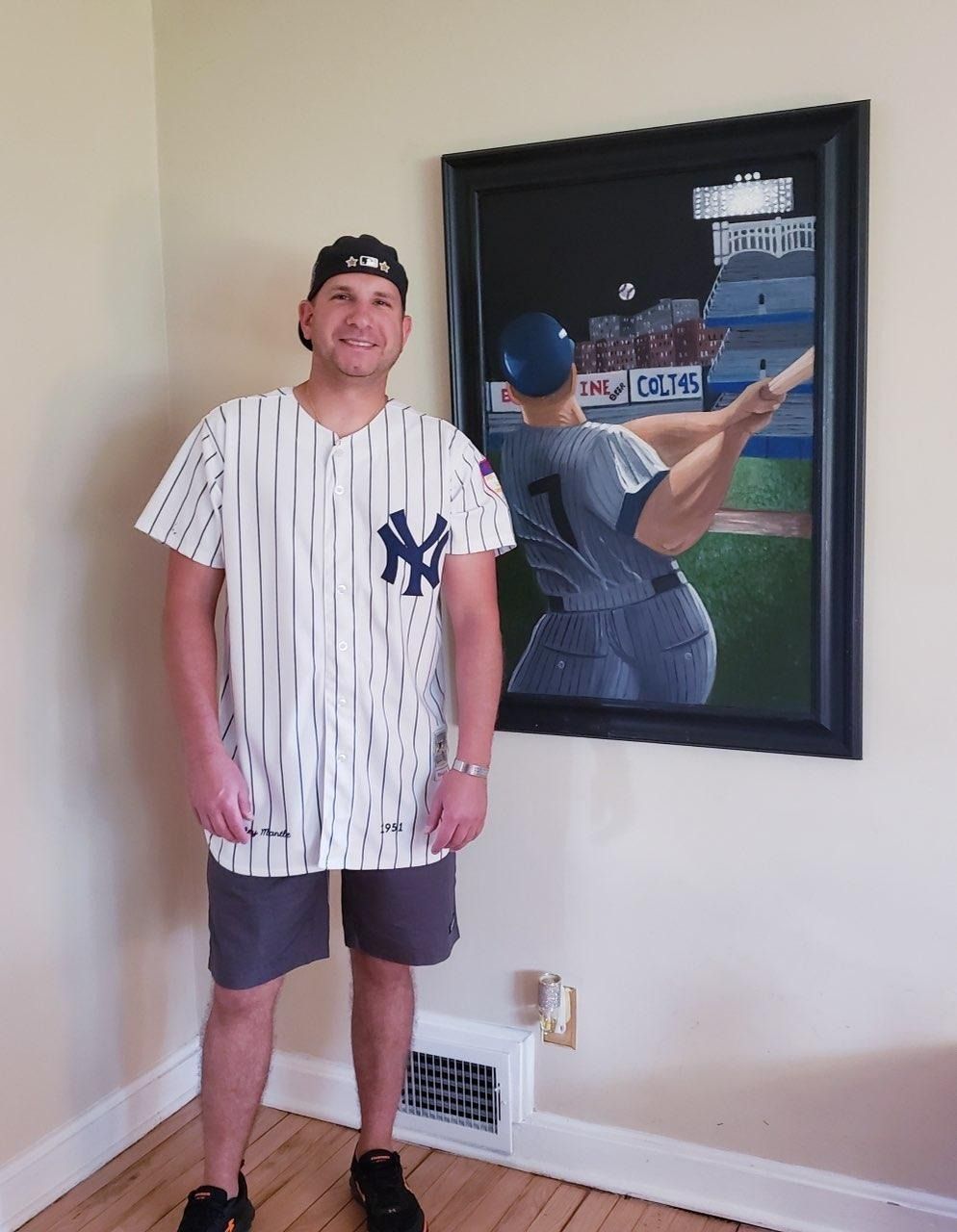 A man in a ny yankees jersey stands in front of a framed picture of a baseball player