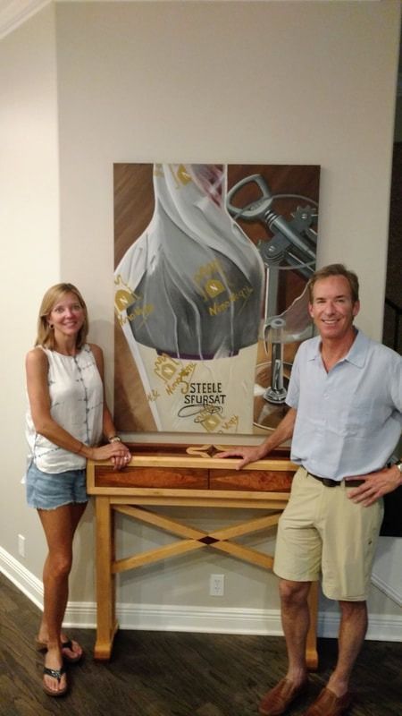 A man and a woman are standing in front of a painting on a wall.