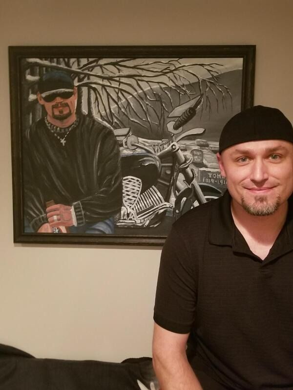 A man is sitting in front of a painting of a man on a motorcycle