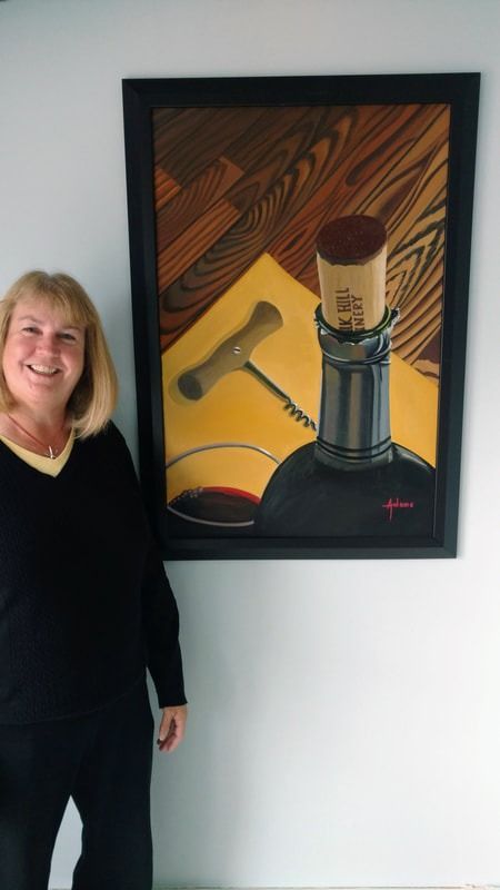 A woman is standing in front of a painting of a bottle of wine and a corkscrew