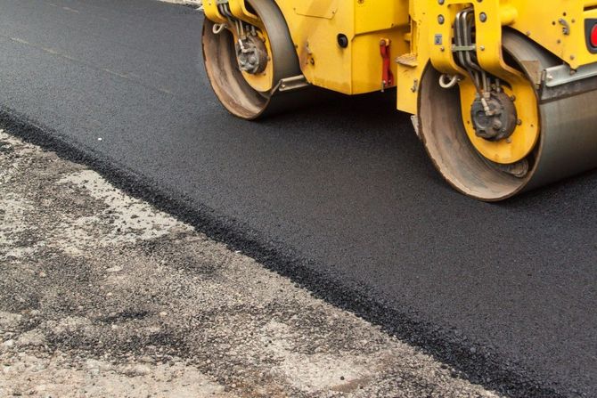 Yellow road roller compacting fresh asphalt on a street edge