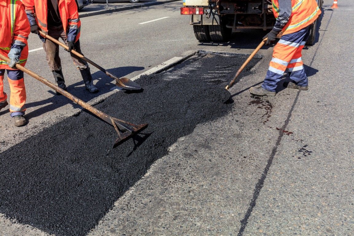 Road workers using rakes to spread fresh asphalt on a road surface