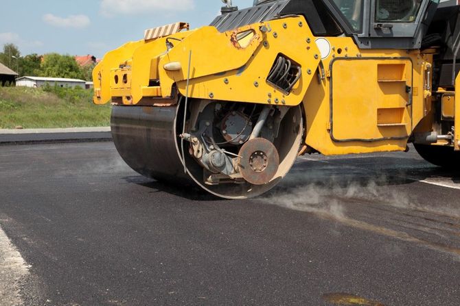 Yellow road roller compacting fresh black asphalt on a road construction site